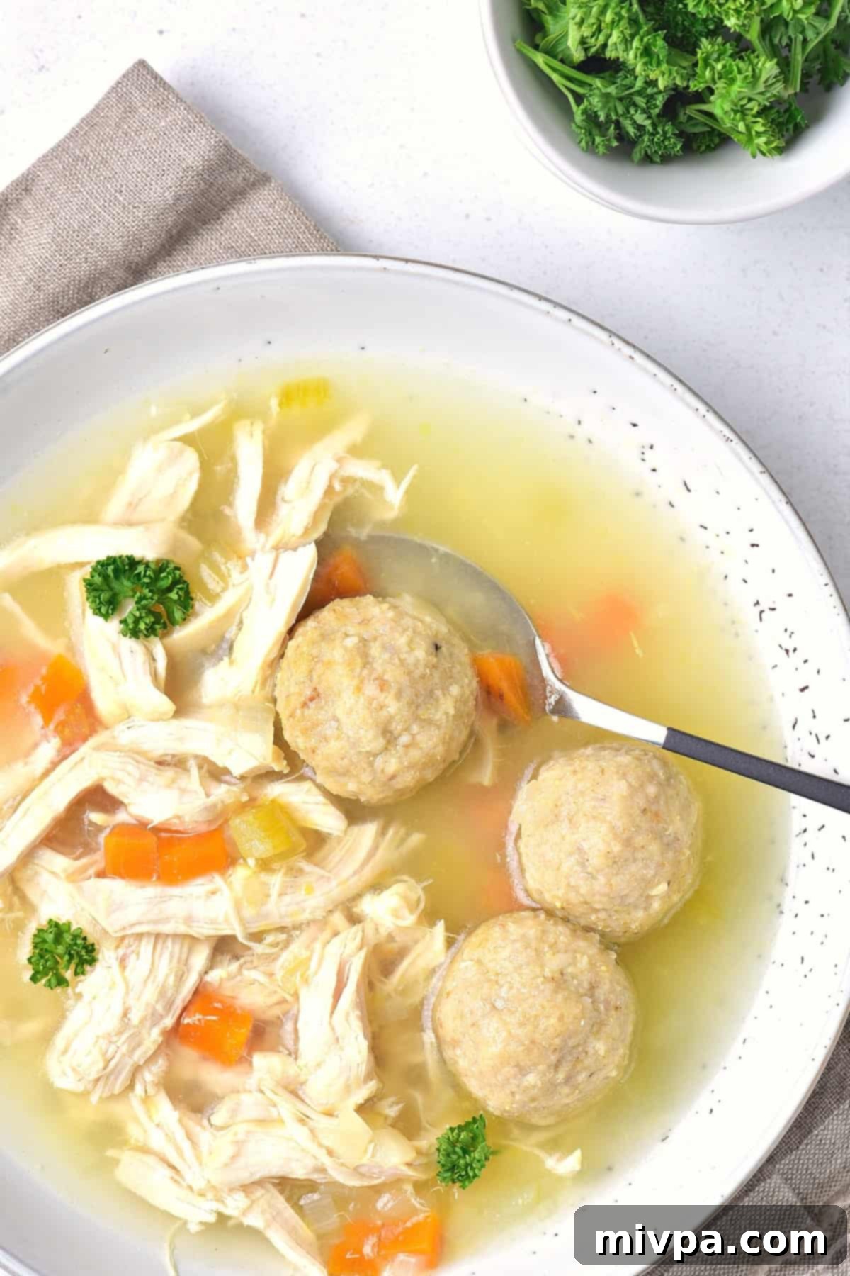 Matzo Ball Soup (Gluten-Free) - Ready to Serve A large, steaming bowl of gluten-free matzo ball soup filled with shredded chicken and matzo balls, garnished with fresh herbs.