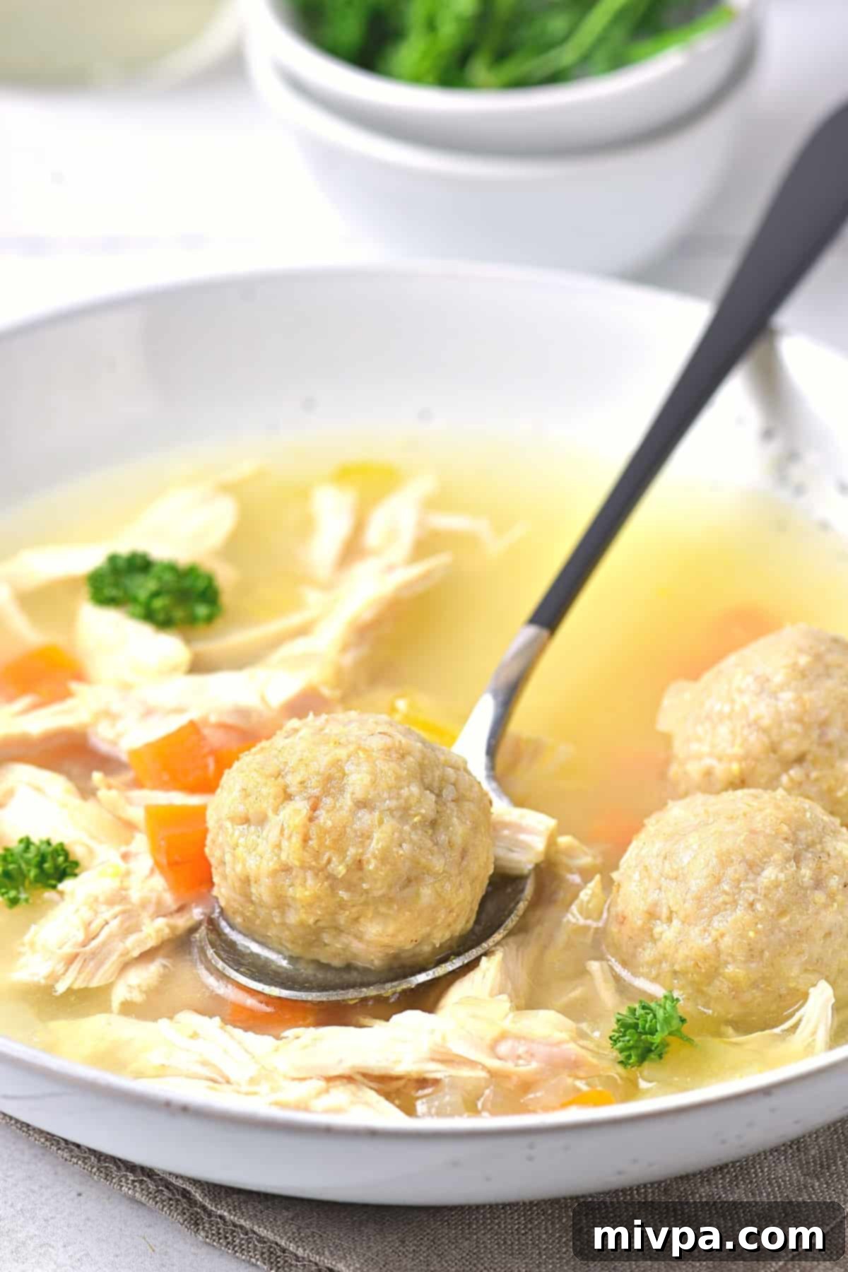Gluten-Free Matzo Ball Soup (Dairy-Free) - Spoon View Spoon lifting a homemade gluten-free matzo ball from a bowl of soup, showing its fluffy texture.