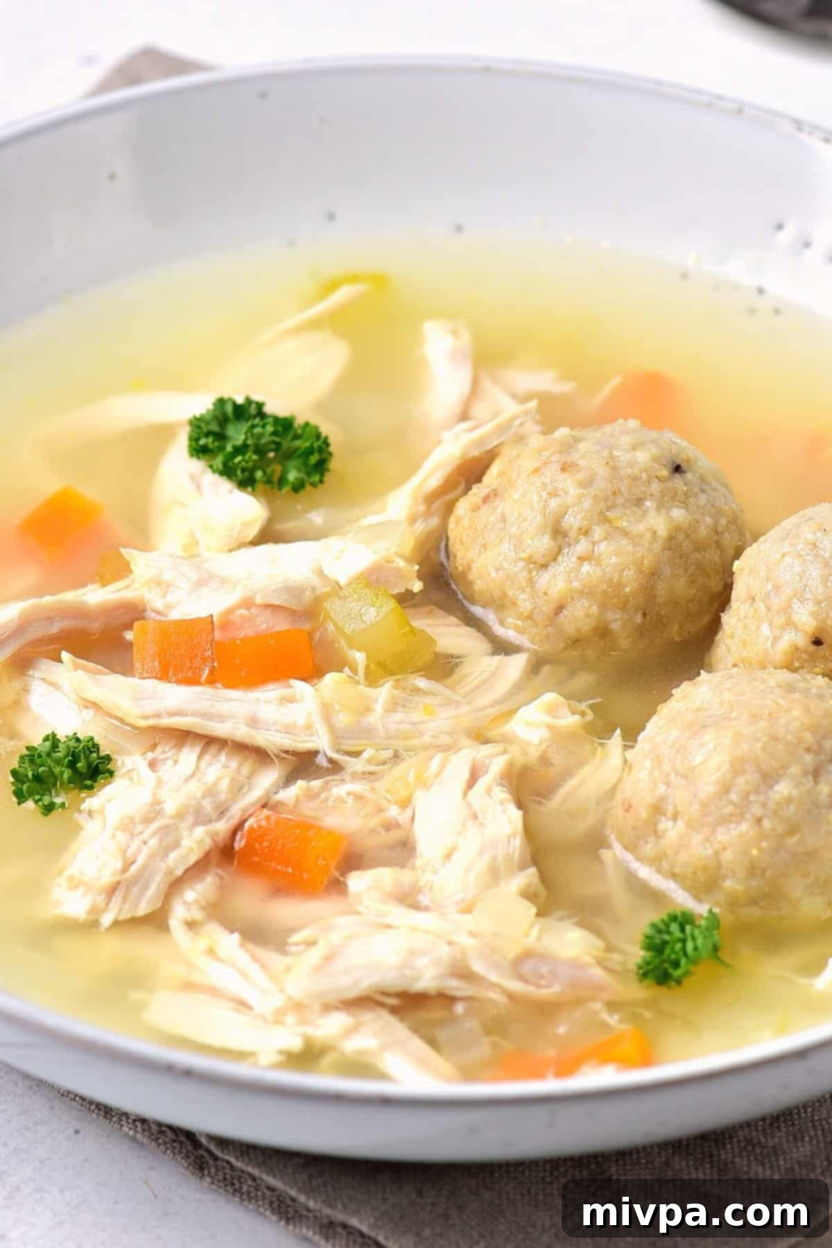Gluten-Free Matzo Ball Soup (Dairy-Free) - Close-up Close up of gluten-free matzo balls and shredded chicken swimming in a rich, clear chicken broth.