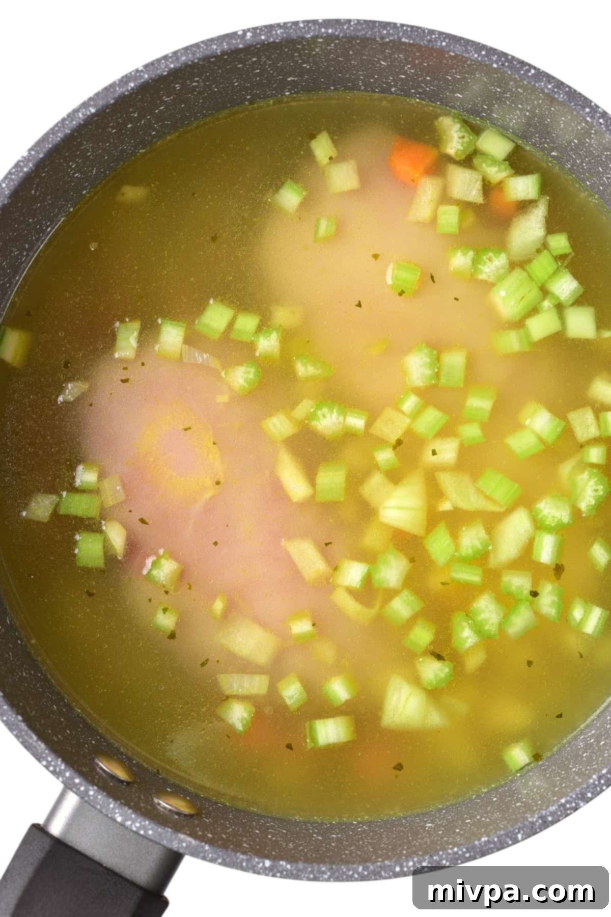 Gluten-Free Matzah Ball Soup (Dairy-Free) - Chicken and Broth Chicken breasts and vegetables simmering in clear chicken broth in a skillet.