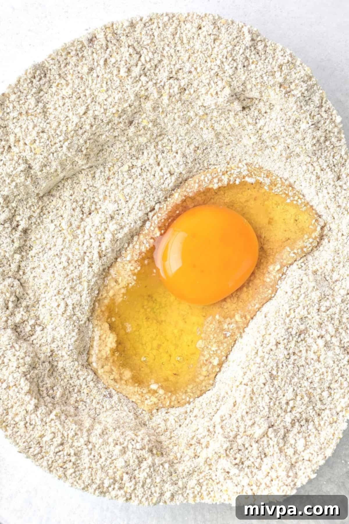 Gluten-Free Matzo Ball Recipe (Dairy-Free) - Mixing Ingredients An egg resting in a well of gluten-free matzo meal in a mixing bowl, ready to be combined.