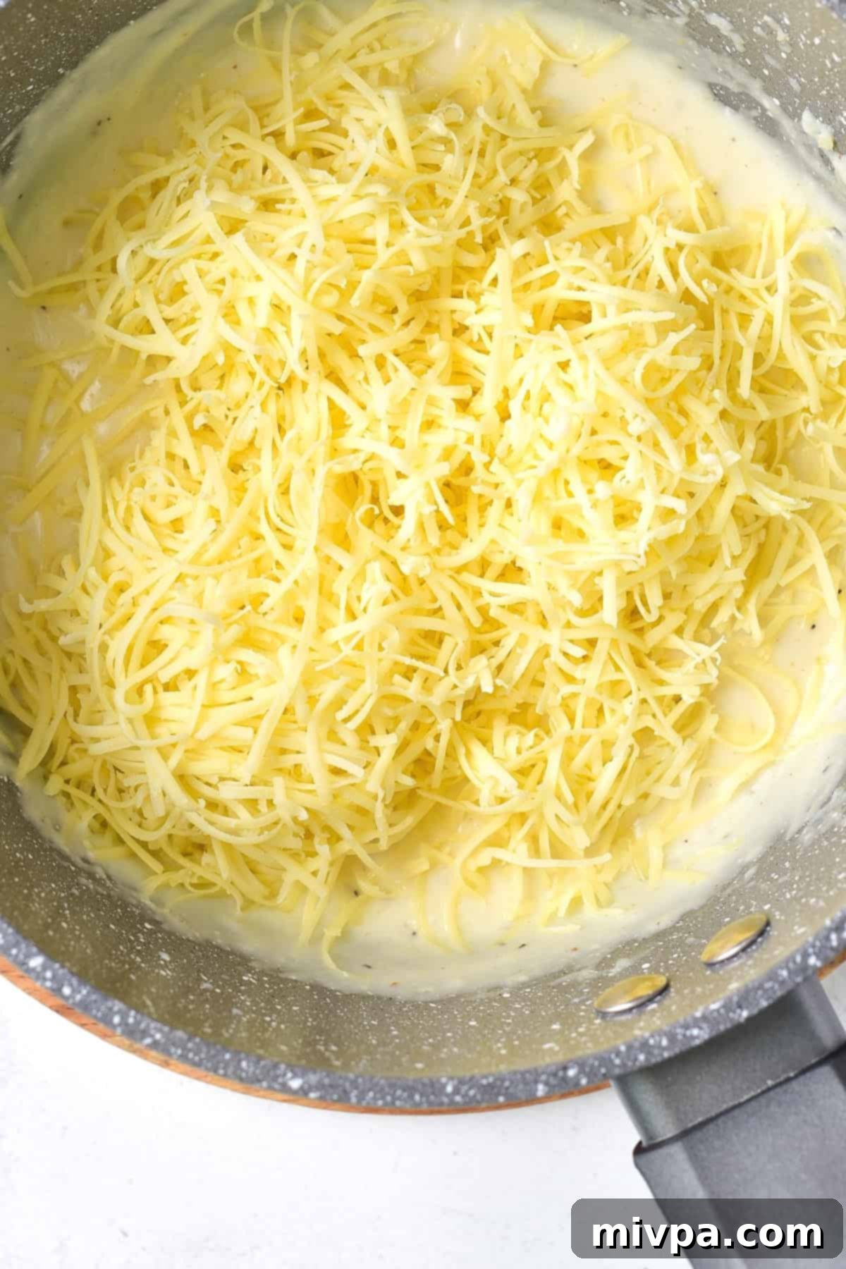Shredded cheese on top of creamy mixture in saucepan.