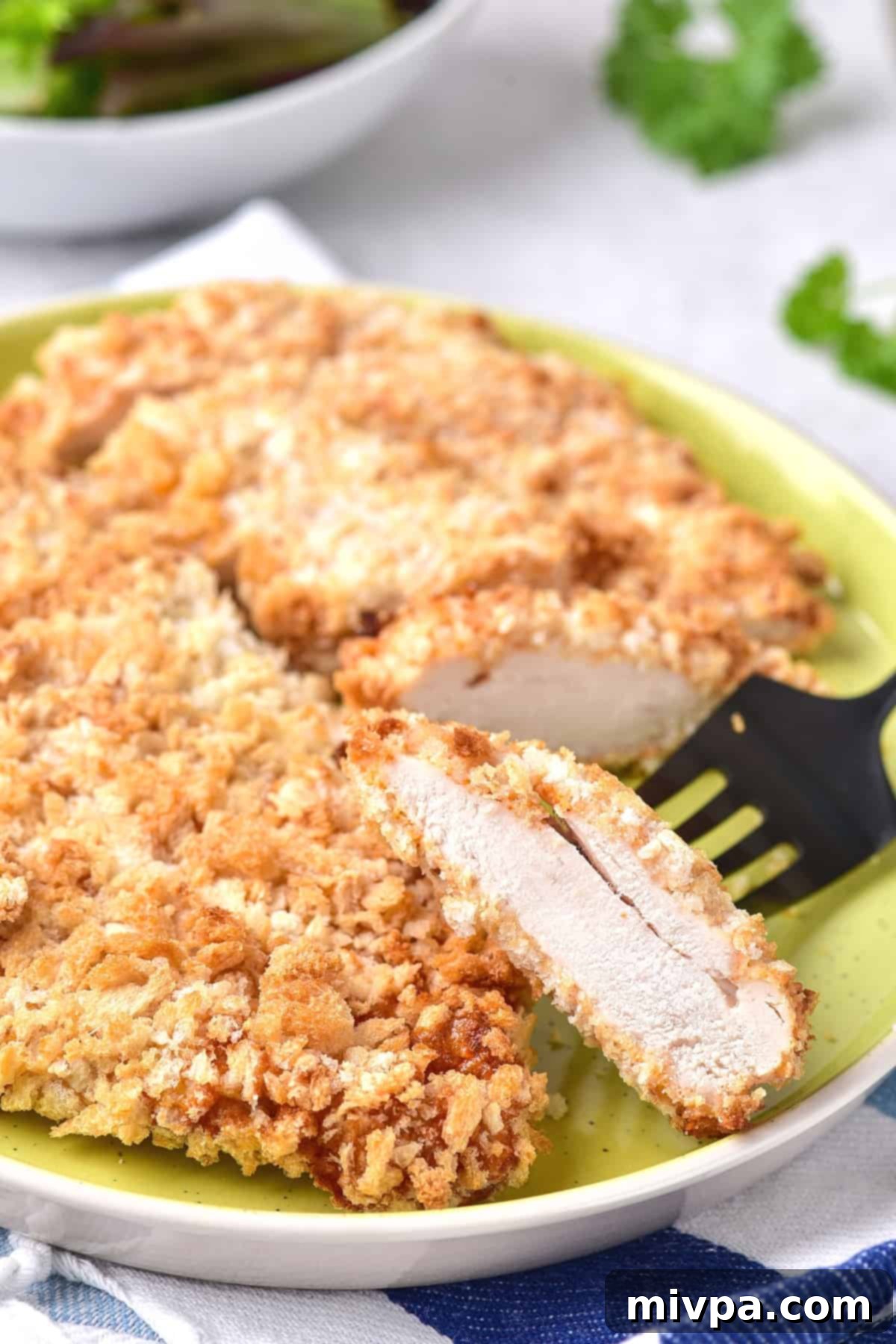 Fork holding up a piece of air fried breaded chicken breast.