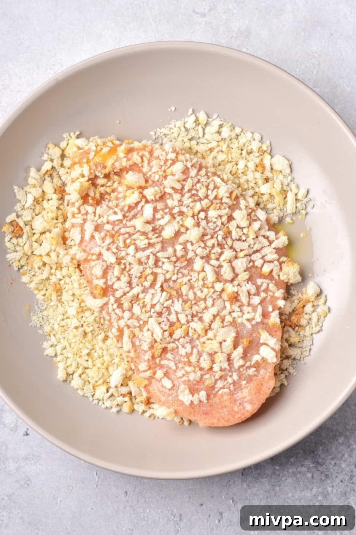Coating chicken cutlet in panko breadcrumbs.