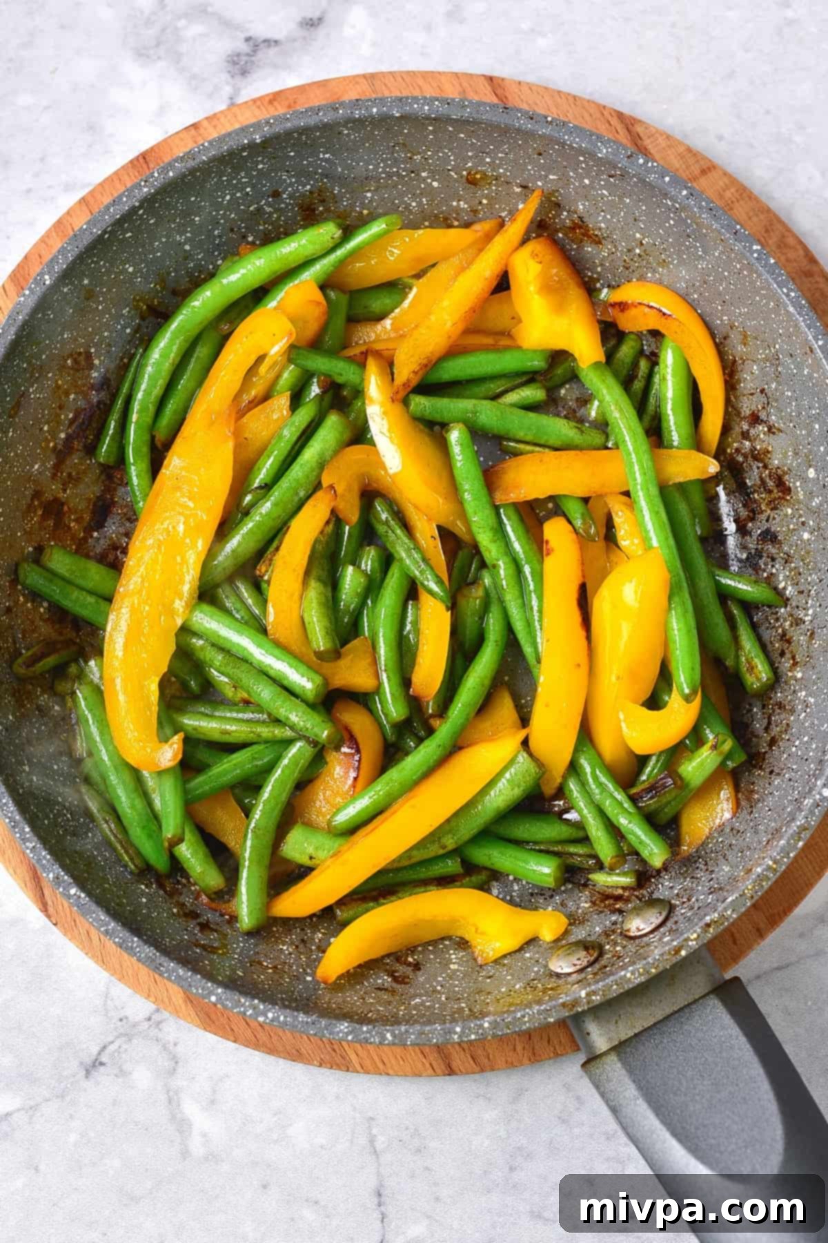 Vibrant yellow bell pepper strips and fresh green beans are stir-frying in a skillet with olive oil over medium-high heat. The vegetables are tender-crisp and maintain their bright colors, showing the careful sautéing process for the honey sesame chicken recipe.