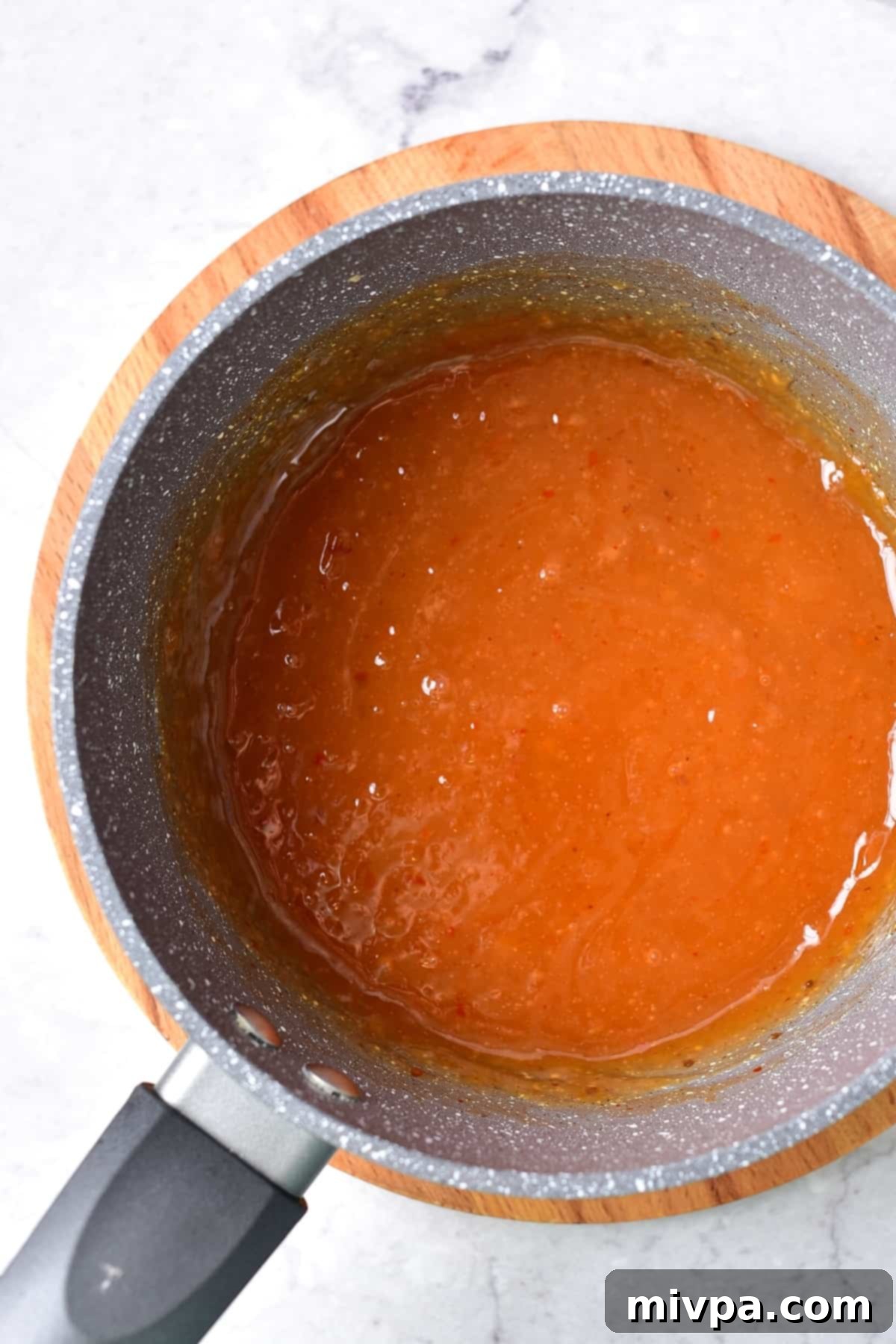 A rich, glossy honey sesame sauce is simmering in a saucepan on the stovetop. The sauce has thickened to a perfect consistency, indicating it's ready to be combined with the chicken and vegetables. This image highlights the crucial step of preparing the flavorful sauce.