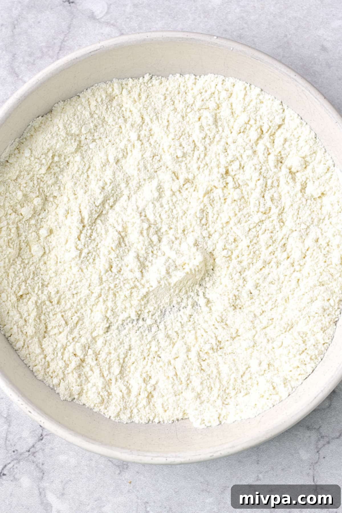 A white bowl holds a perfectly blended flour mixture, consisting of gluten-free all-purpose flour, cornstarch, and baking soda. The dry ingredients are evenly whisked, showing a fine, consistent texture, ready to coat the chicken strips for a crispy, gluten-free finish.