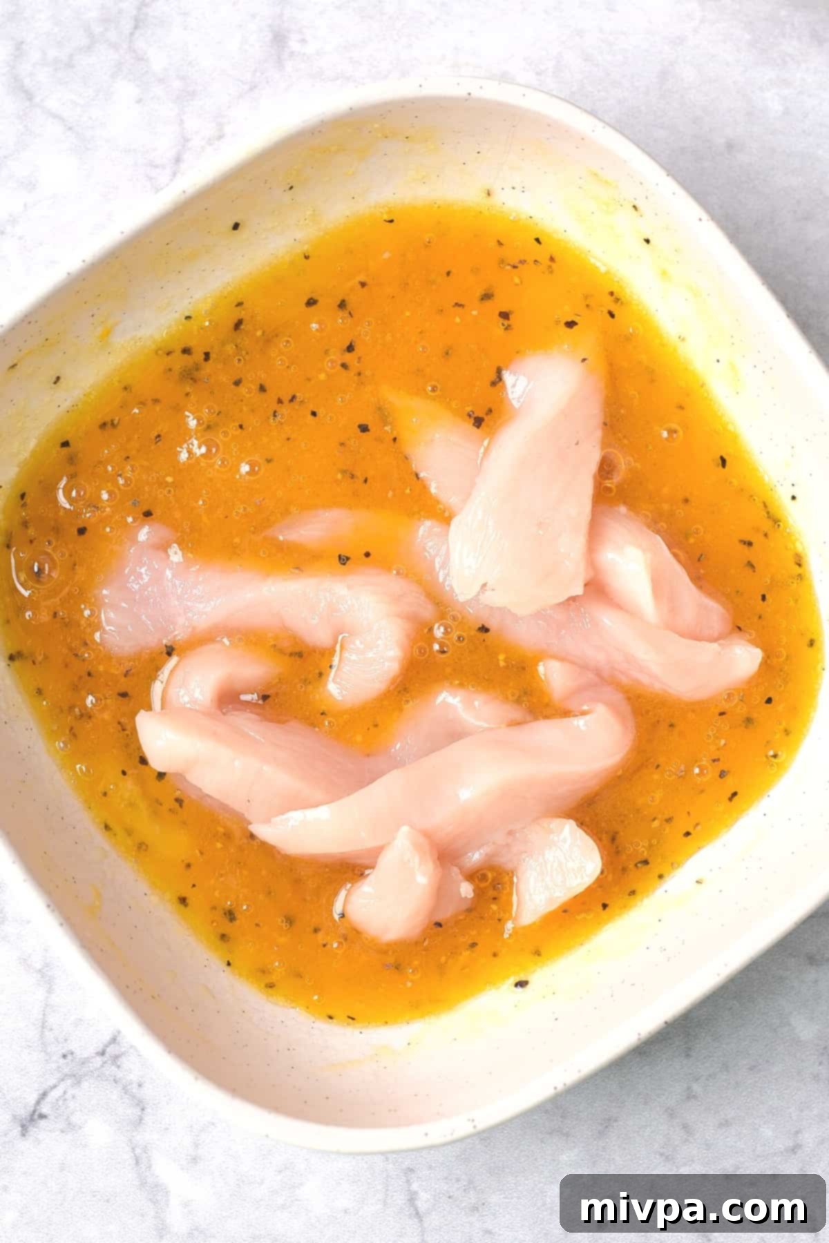 Several chicken strips are immersed in a bowl of the beaten egg mixture, ensuring each piece is thoroughly coated before moving to the next step. The texture of the egg mixture evenly covers the chicken, indicating proper preparation for a crispy coating.