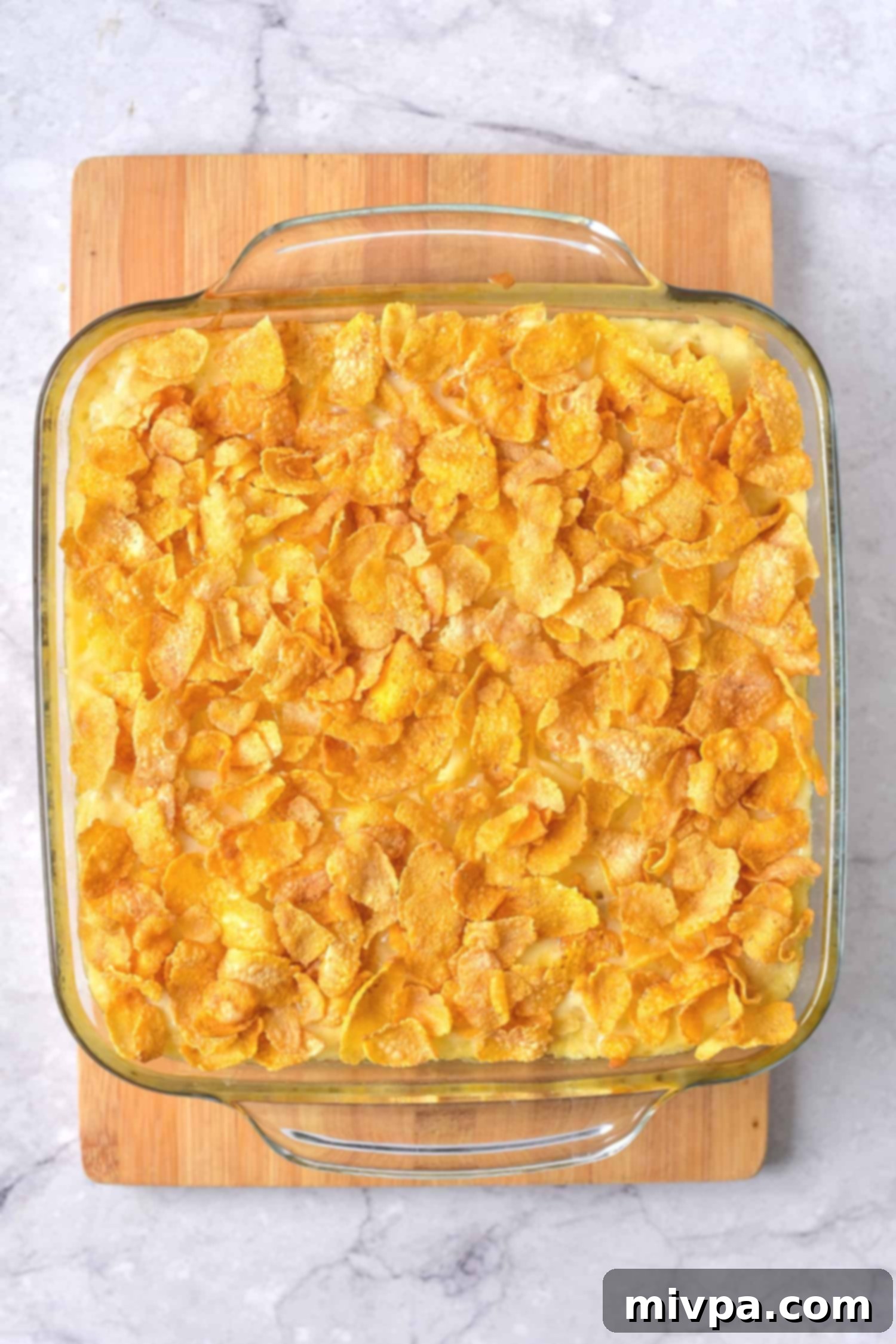 Casserole topped with corn flakes in a glass baking dish, nearly finished baking.