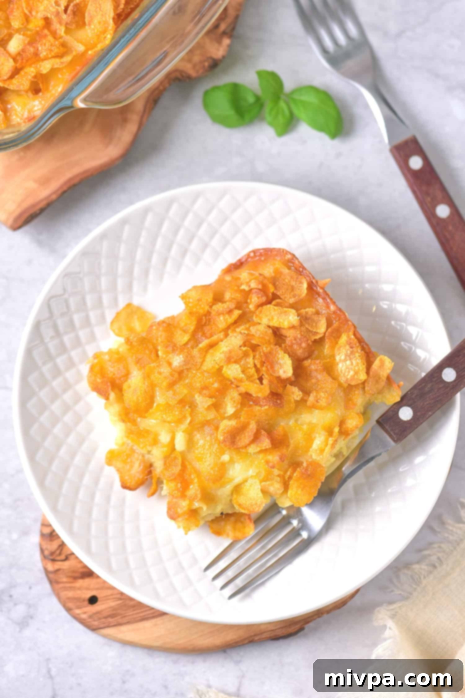 An individual portion of hash brown casserole on a white plate, ready to be eaten.