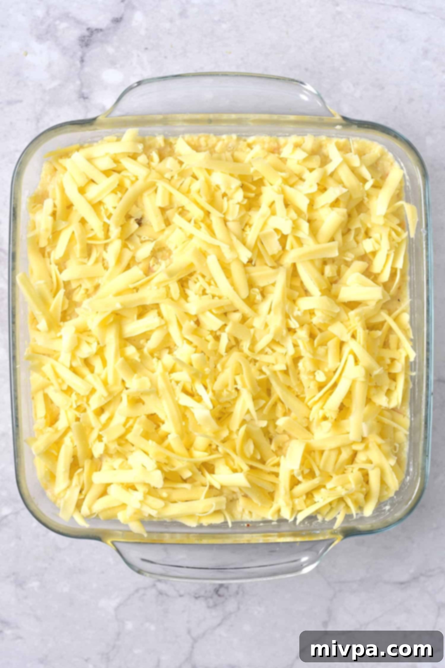 Cheese-topped casserole in a baking dish, ready to be baked.