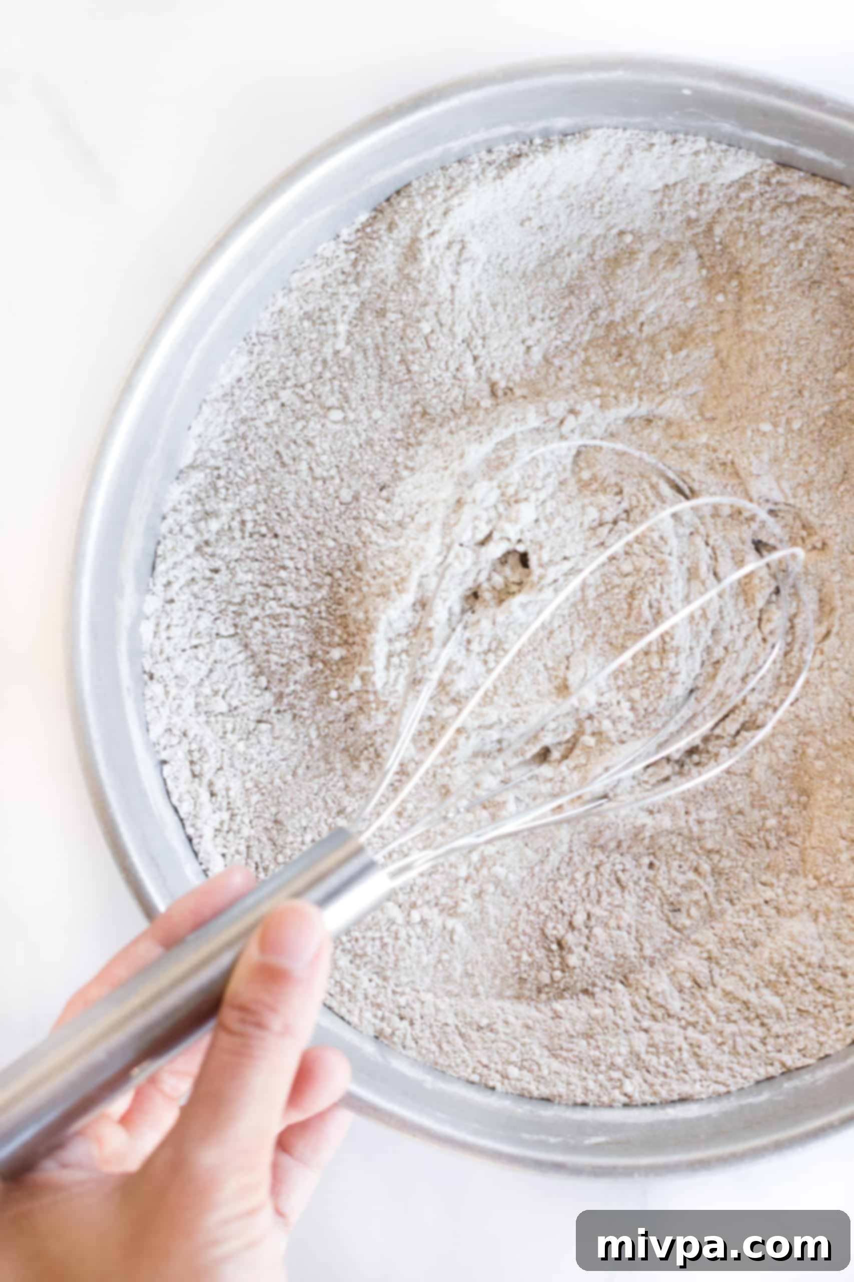 Whisking a mixture of dry ingredients in a sleek metal mixing bowl.