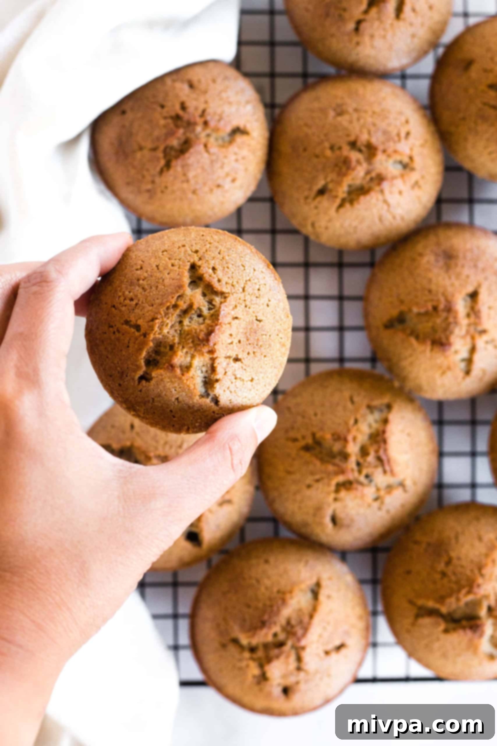 A hand gently lifting a warm muffin from a wire rack, ready to be enjoyed.