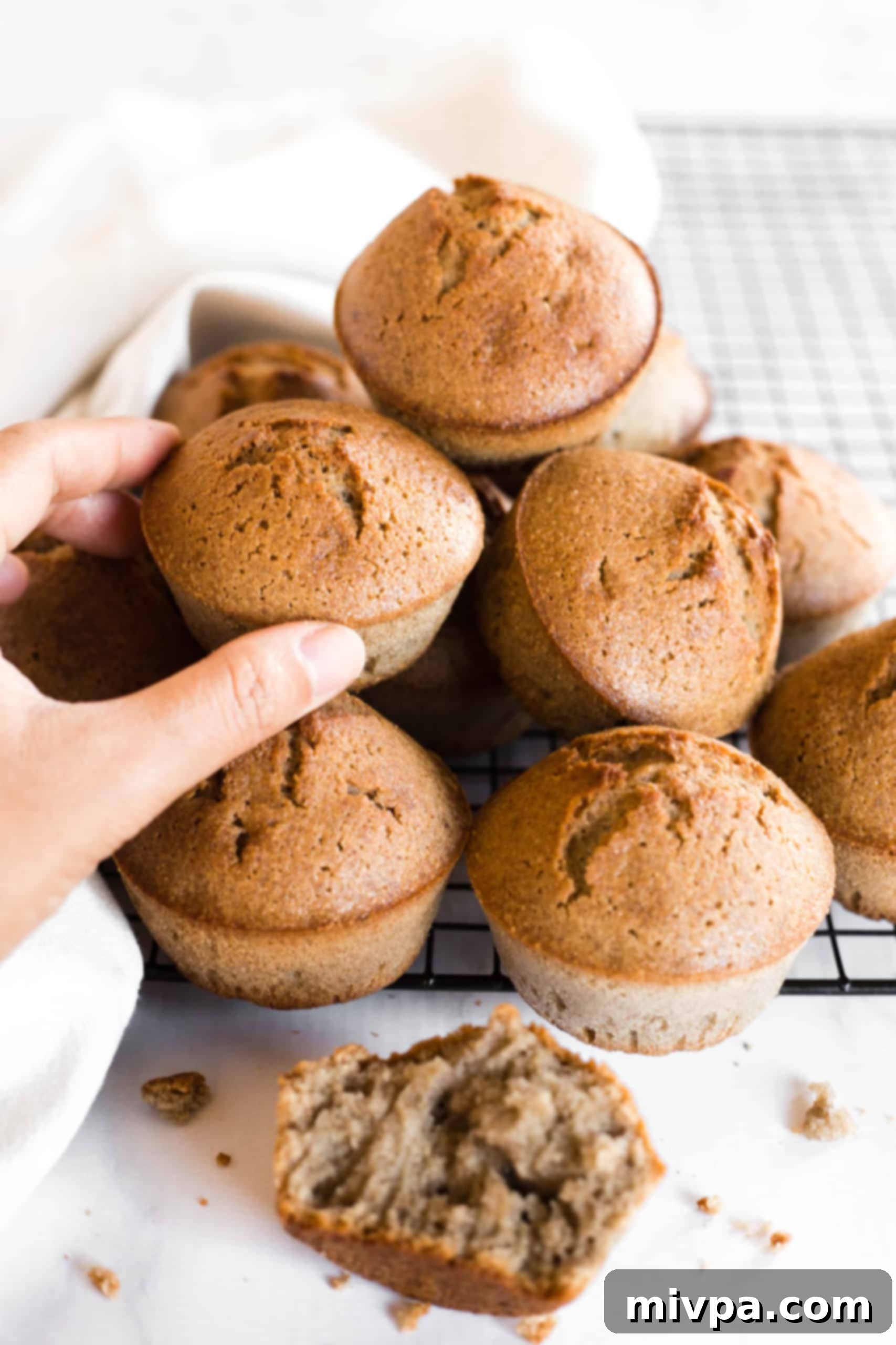 A hand reaching for a buckwheat muffin from a tempting stack of muffins on a wire rack.