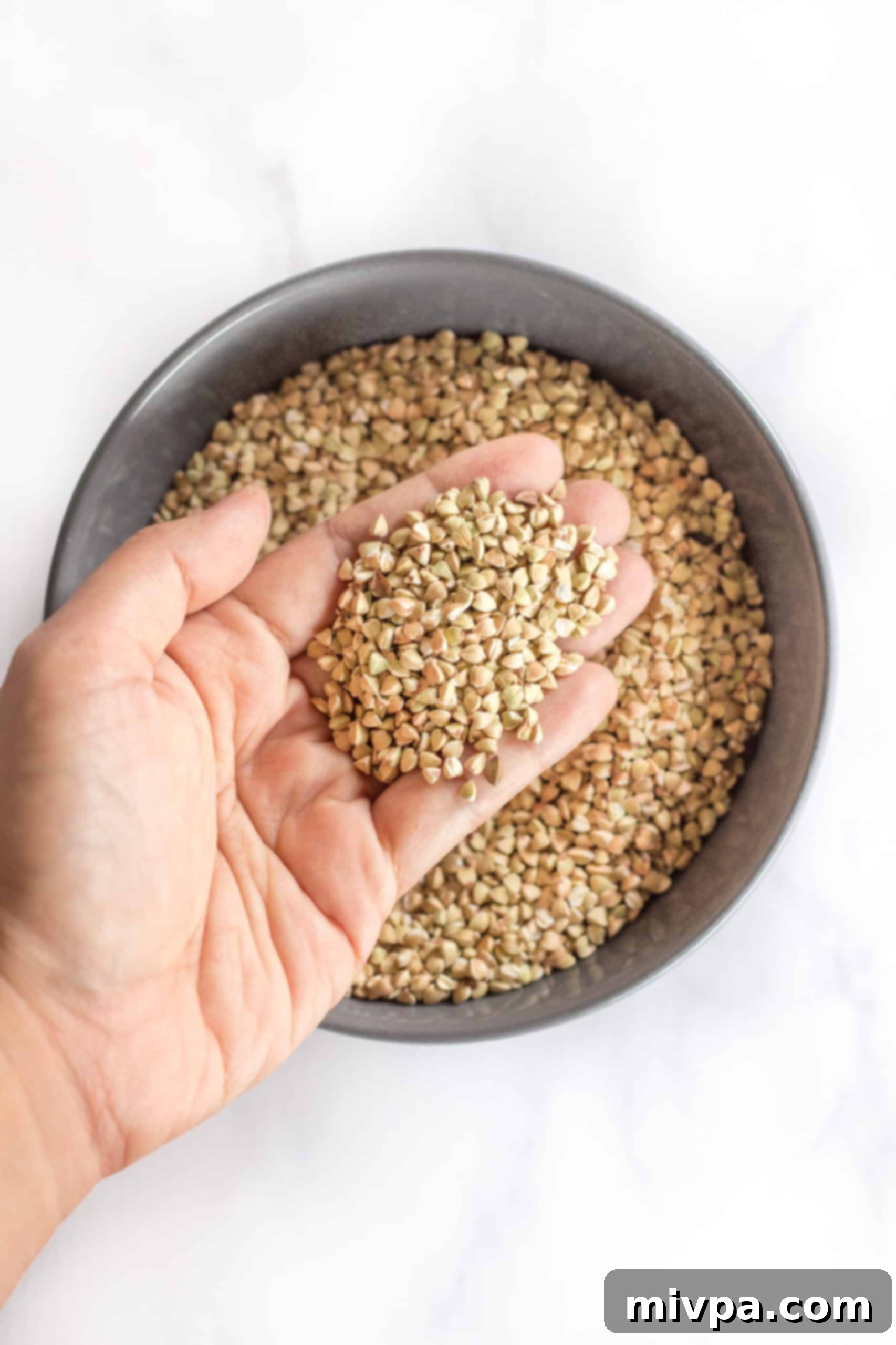 A hand holding up hulled buckwheat groats, showcasing their natural, light color.