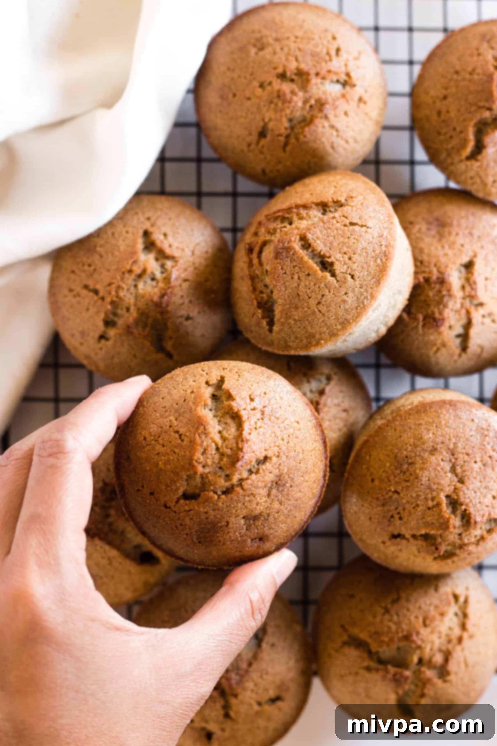 A hand holding up a freshly baked buckwheat muffin from a wire rack.