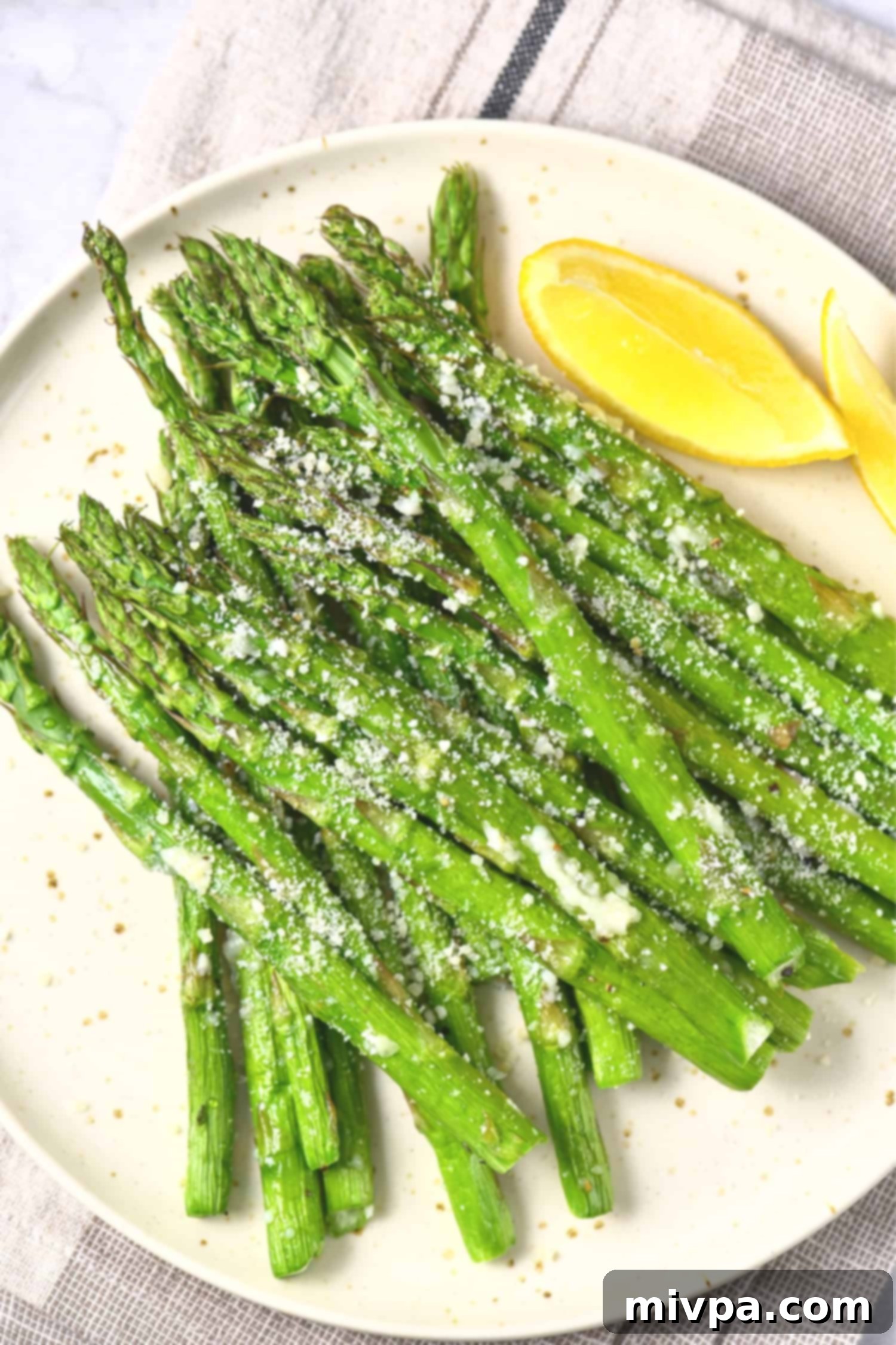 A plate of air fryer parmesan asparagus and lemon wedges, ready to be served.