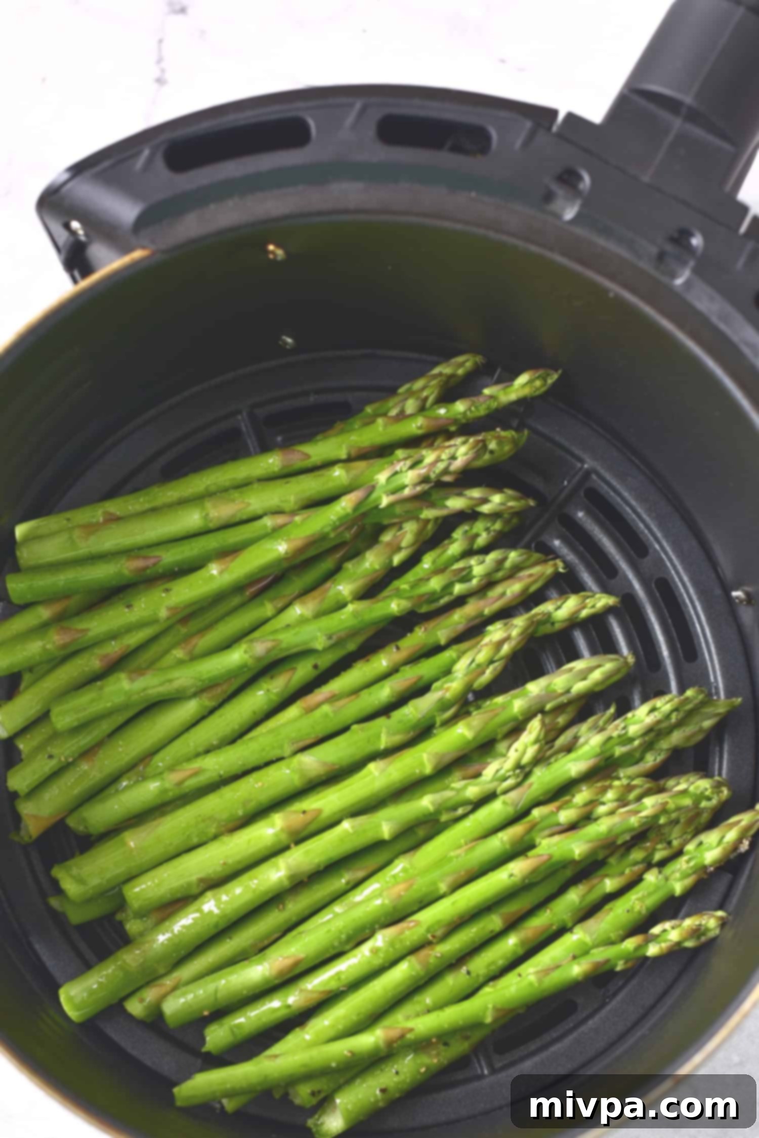 Seasoned asparagus stalks arranged in a single layer in the air fryer basket, ready for cooking.