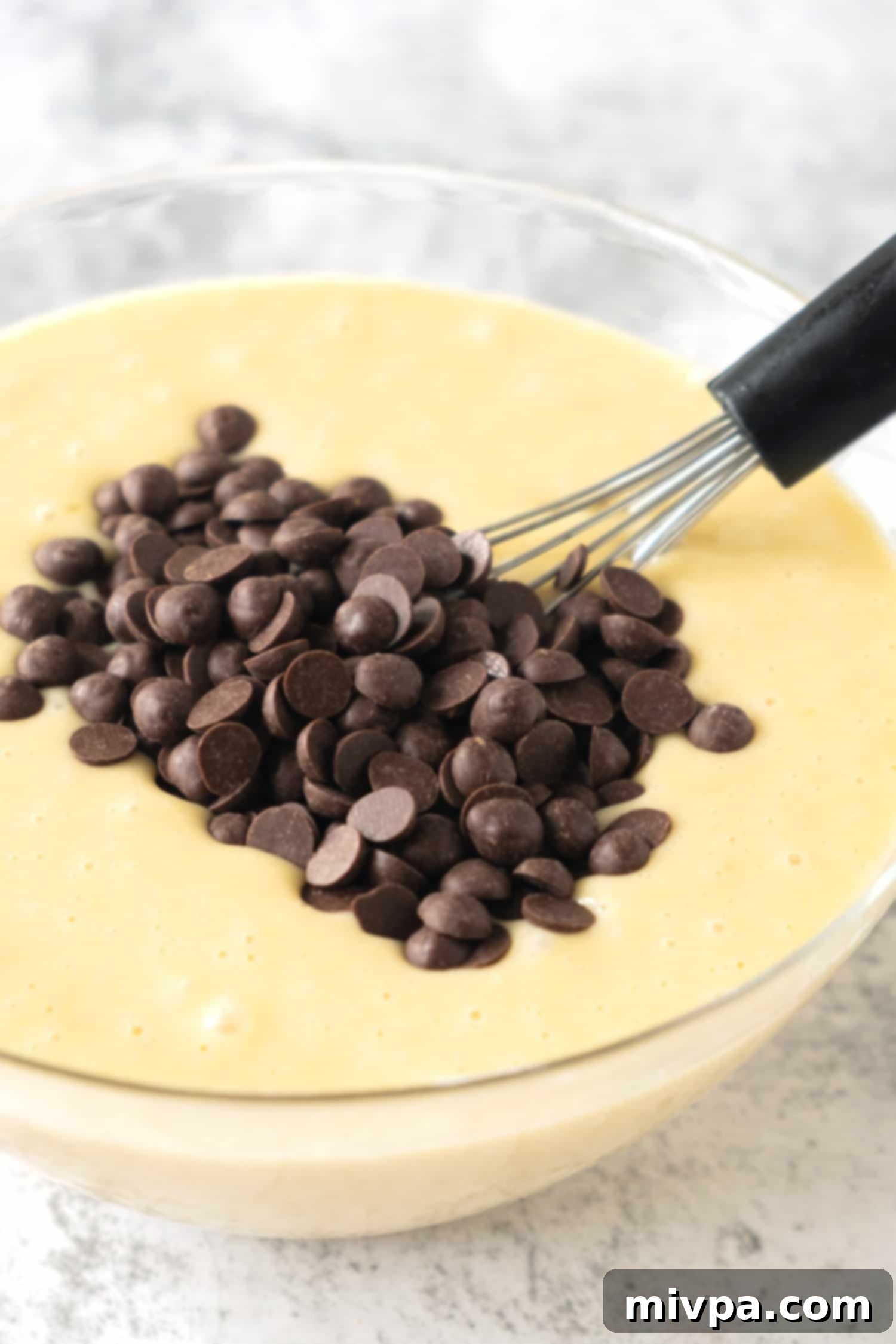 Gluten-Free Chocolate Chip Muffins (Dairy-Free) Dairy-free chocolate chips sprinkled on top of a bowl of thick muffin batter, ready to be folded in.