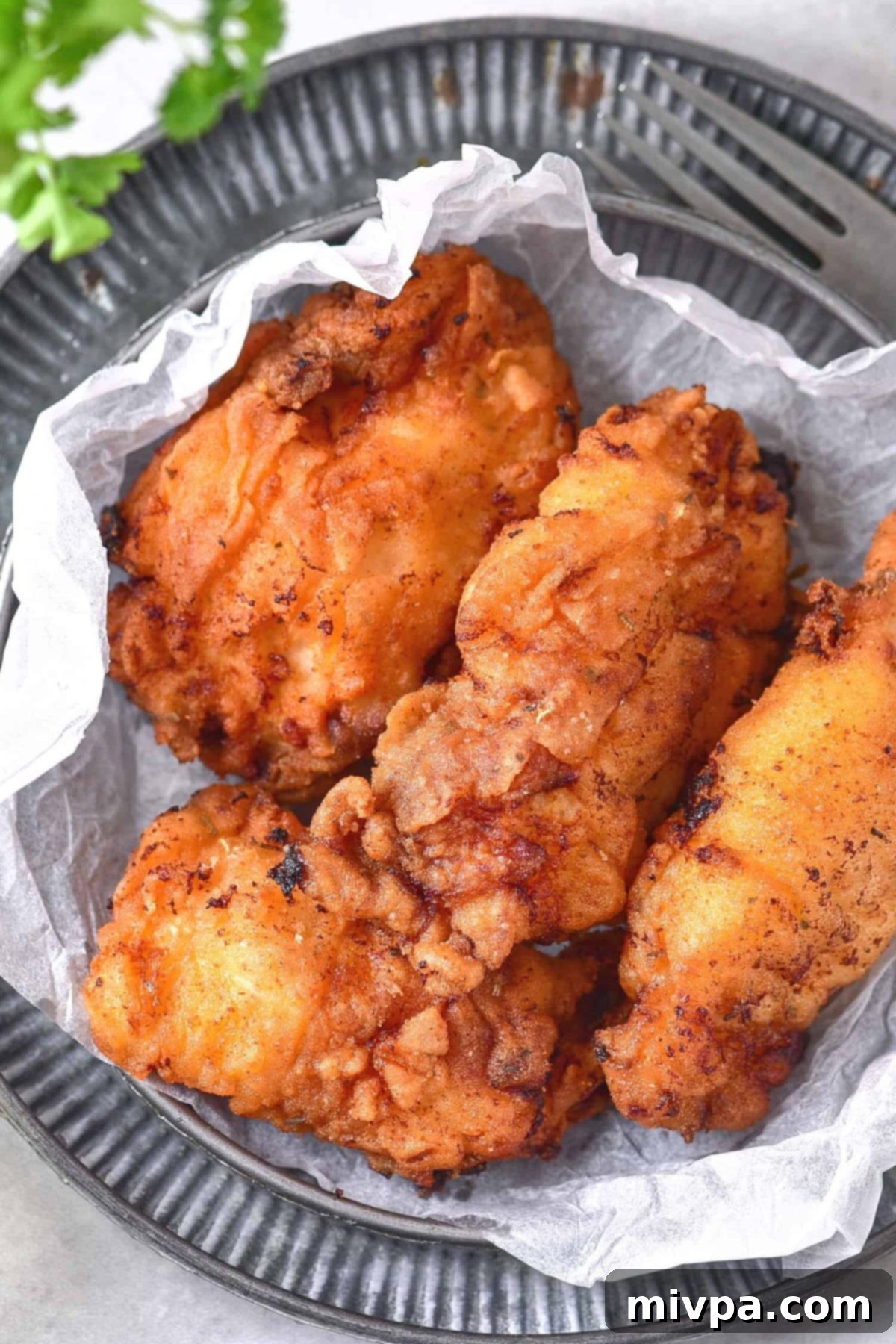 Gluten-Free Fried Chicken Recipe (Dairy-Free) A plate of golden brown, crispy gluten-free fried chicken served on parchment paper with a sprinkle of fresh parsley.