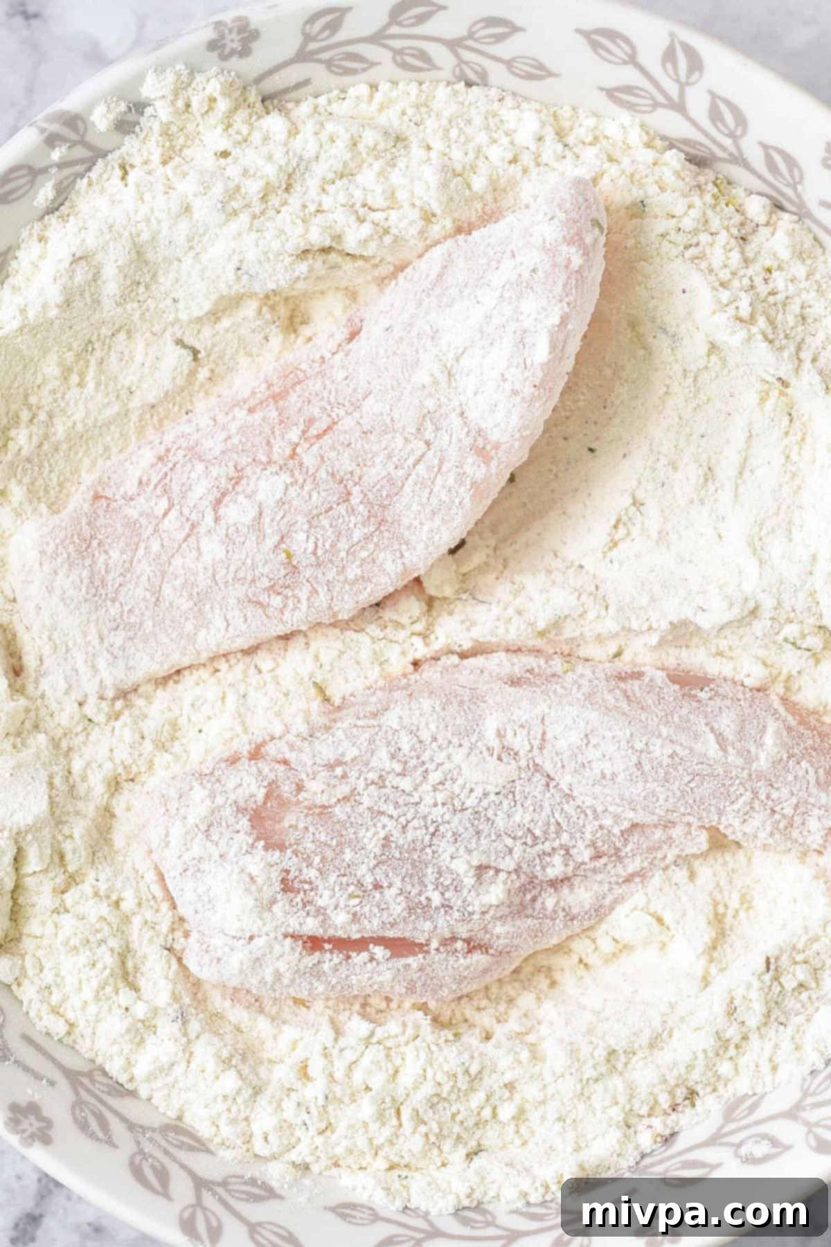 How to Make Gluten-Free Fried Chicken (Dairy-Free) A hand coating a piece of chicken in the seasoned flour mixture, ensuring full coverage.