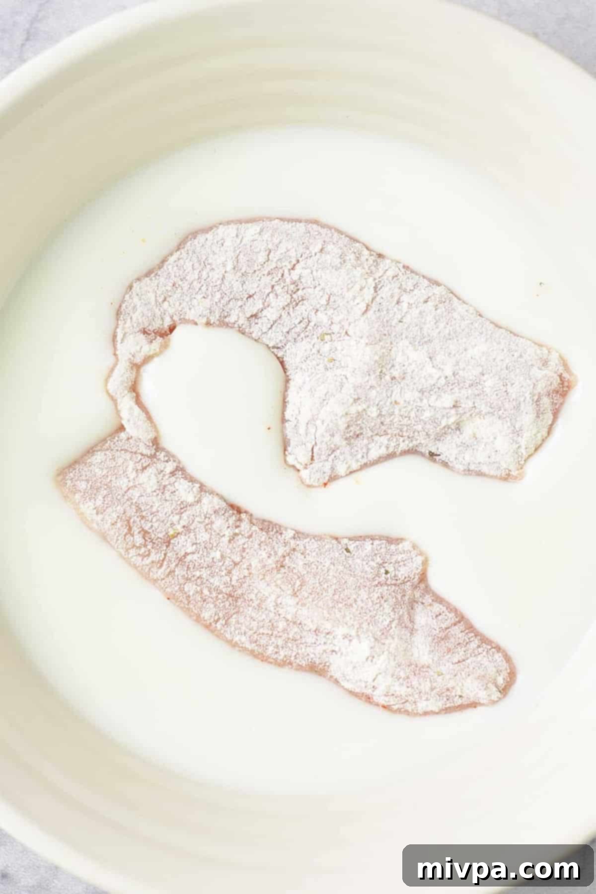 Dairy-Free Fried Chicken Recipe Flour-coated chicken strips submerged in dairy-free buttermilk, ensuring thorough coverage.