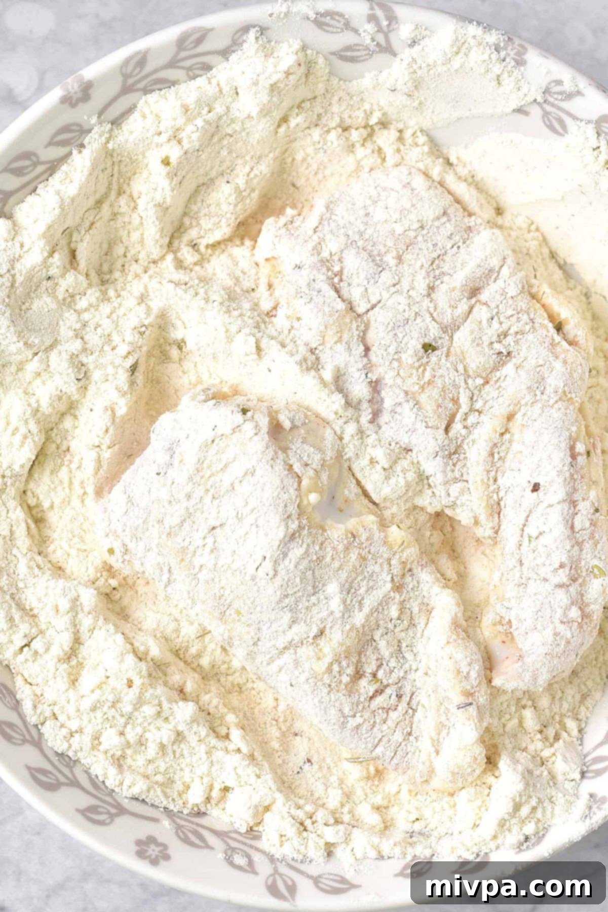 Gluten-Free Fried Chicken (Dairy-Free) A piece of buttermilk-soaked chicken being coated for the second time in the seasoned flour mixture, creating a thick crust.
