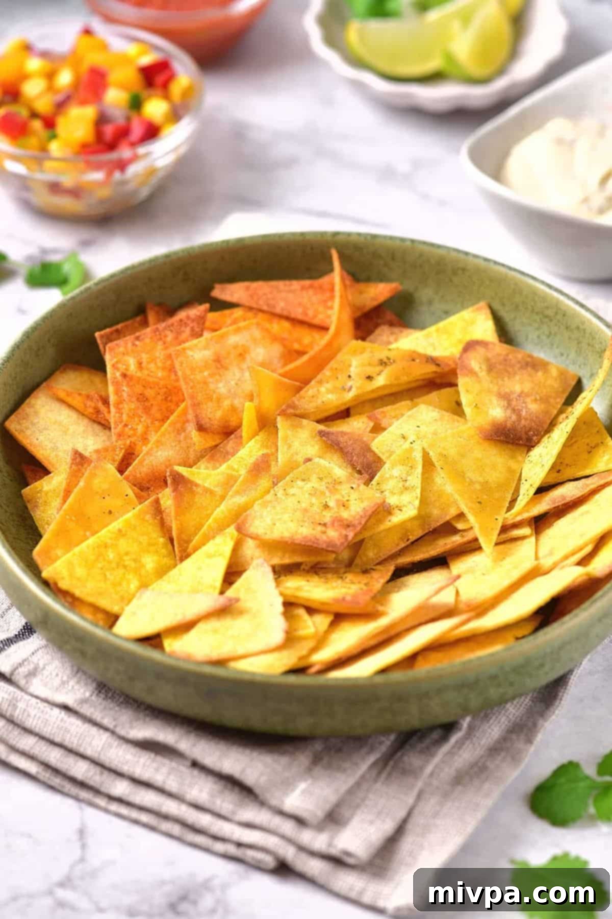 A bowl of tortilla chips with bowls of salsa in the background.