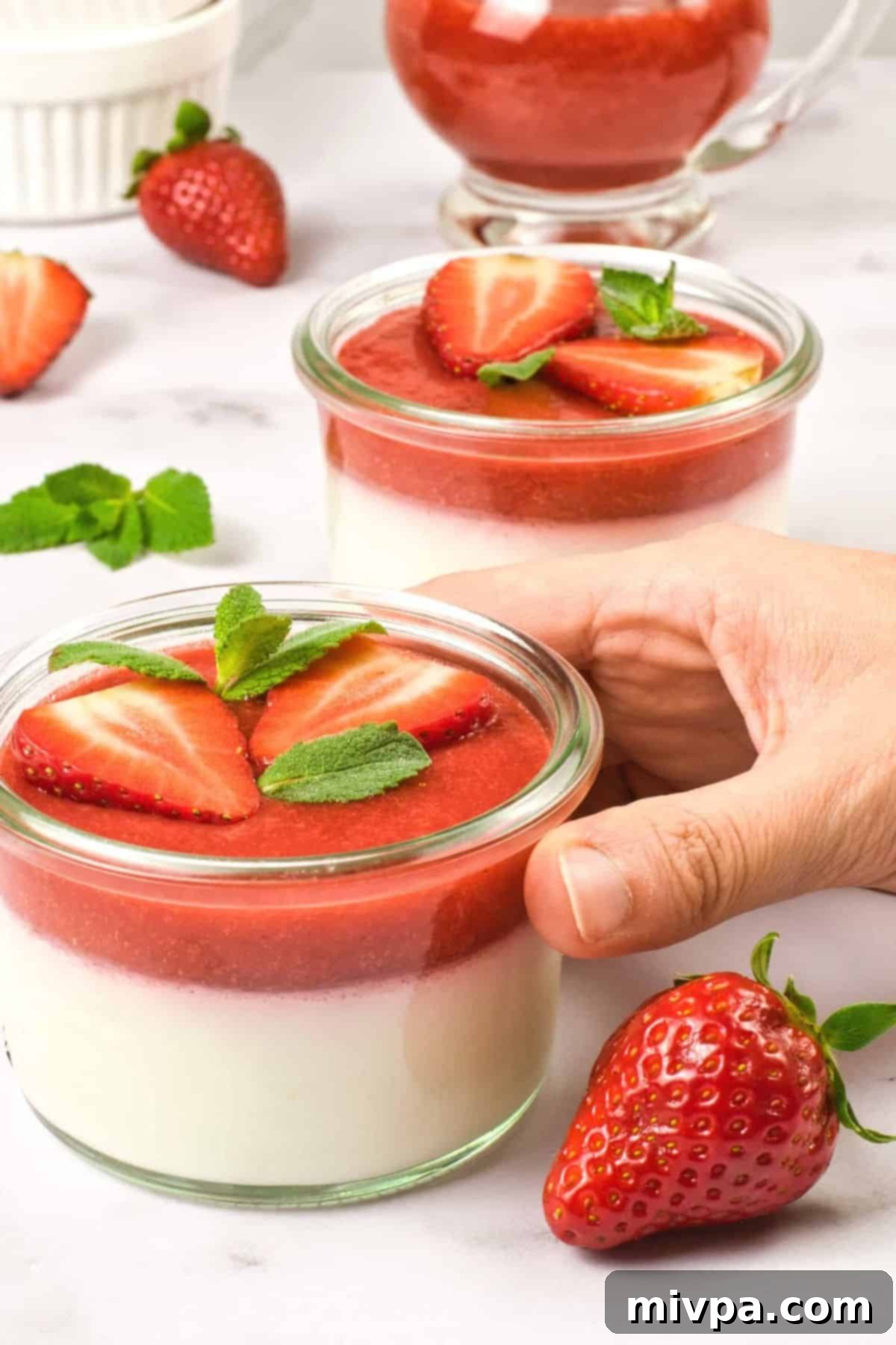 Creamy Coconut Panna Cotta (Gluten-Free, Vegan) Holding a jar with coconut panna cotta topped with strawberry sauce.