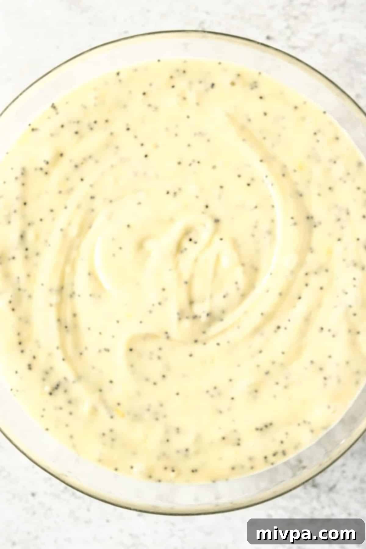 Gluten-Free Lemon Poppyseed Muffins (Dairy-Free) Poppy seed muffin batter, thick and pale yellow, in a glass bowl after wet and dry ingredients have been mixed.