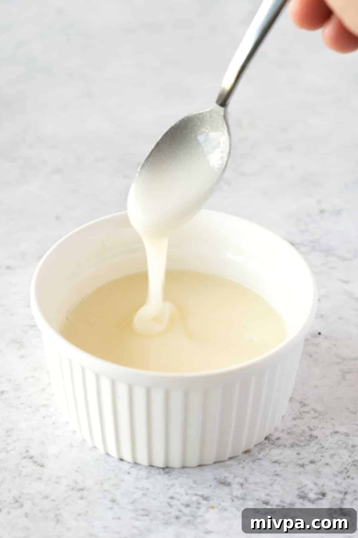 Gluten-Free Lemon Poppy Seed Muffins (Dairy-Free) A spoon dripping with a perfectly thick and glossy lemon glaze, ready to be drizzled over the muffins.