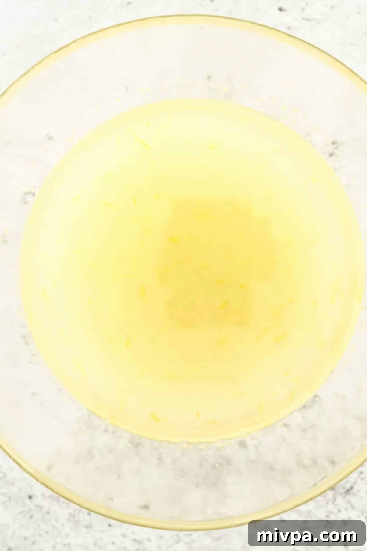 Dairy-Free Lemon Poppy Seed Muffins (Gluten-Free) A glass bowl containing a vibrant yellow mixture of sugar, oil, and fresh lemon zest, ready for the next step.