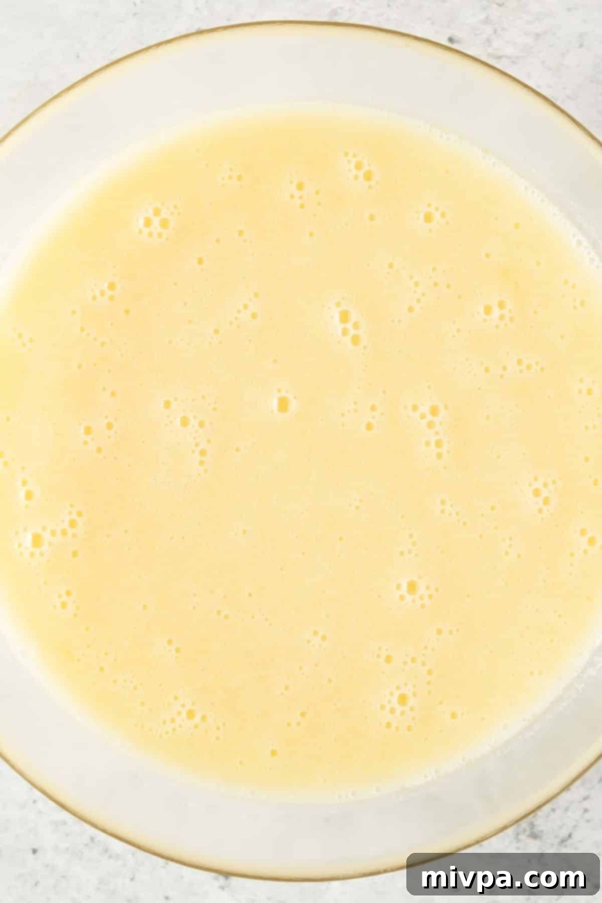 Gluten-Free Lemon Poppy Seed Muffins (Dairy-Free) A pale yellow, frothy mixture in a glass bowl after eggs, lemon juice, and almond milk have been whisked in.