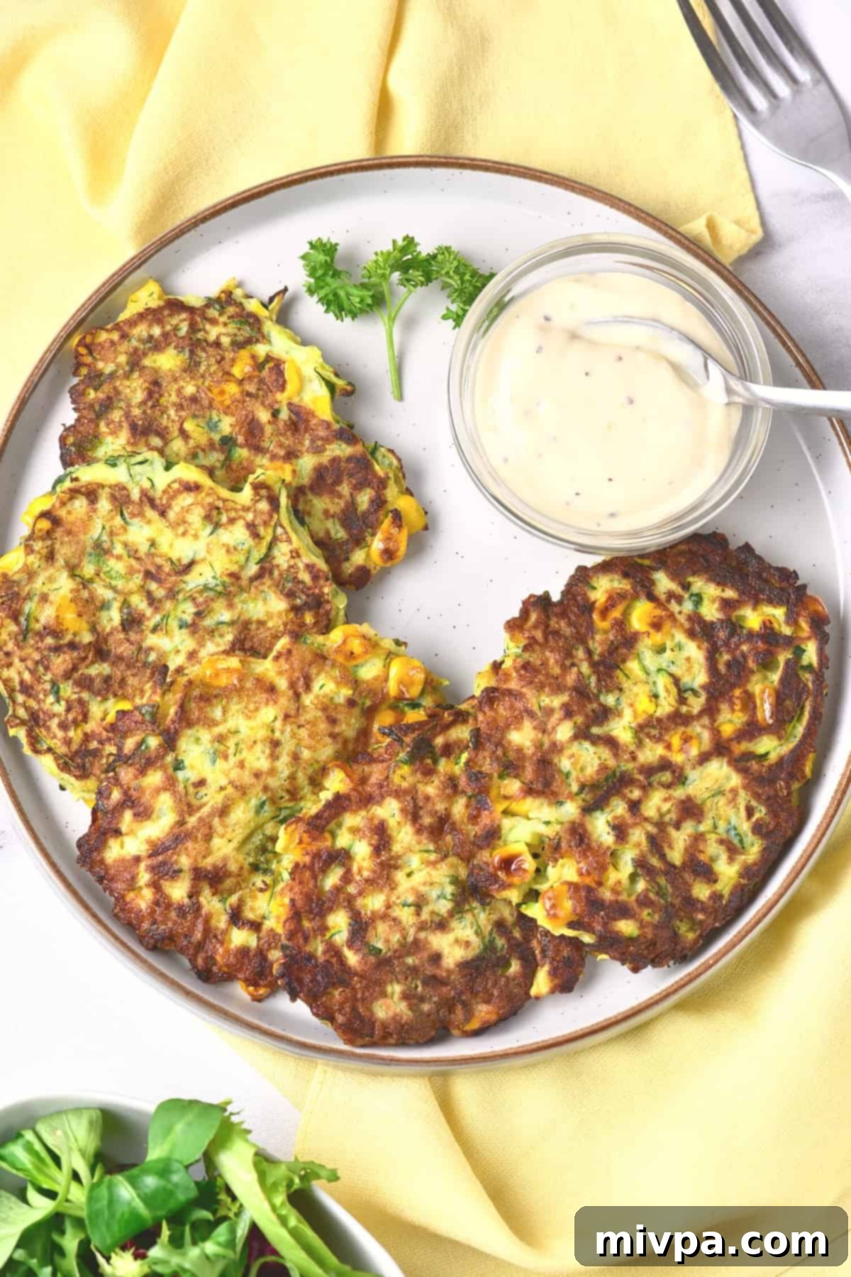 Top down view of zucchini fritters and garlic aioli on a plate.