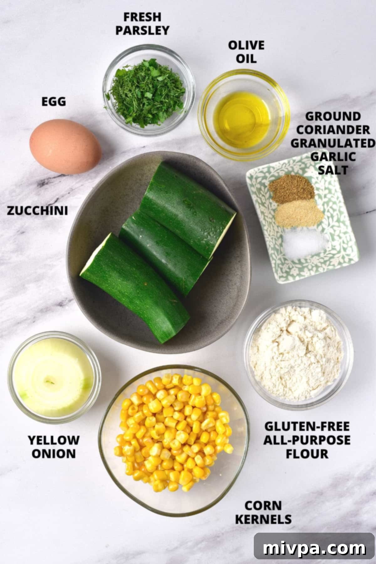 Ingredients for gluten-free zucchini fritters recipe laid out on marble board.