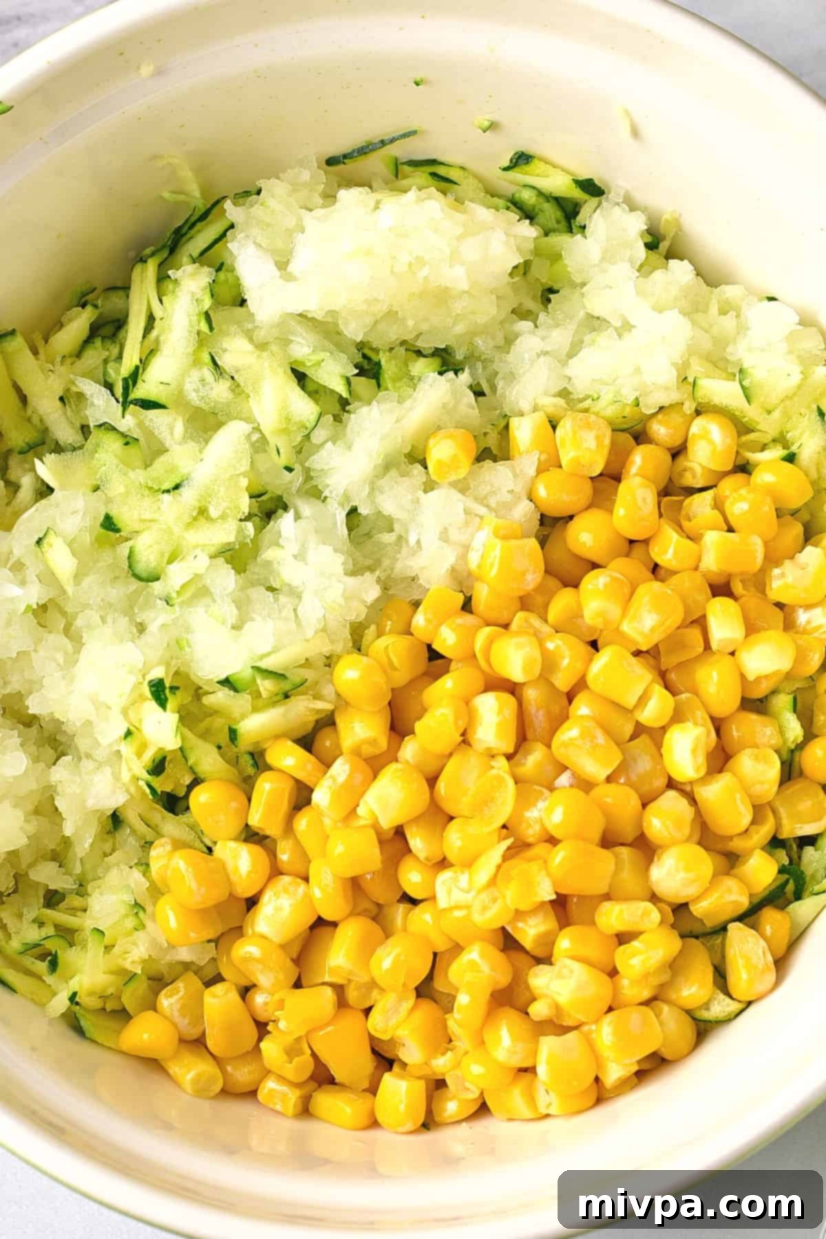 A bowl of grated zucchini, grated onion and sweet corn kernels.