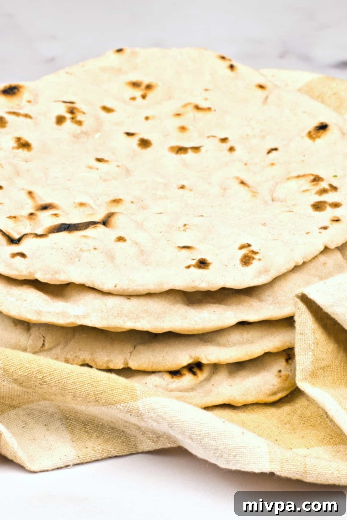 Gluten-Free Pita Bread Recipe (Dairy-Free, Vegan) A stack of gluten-free pita bread on kitchen towel, showcasing its perfect texture.