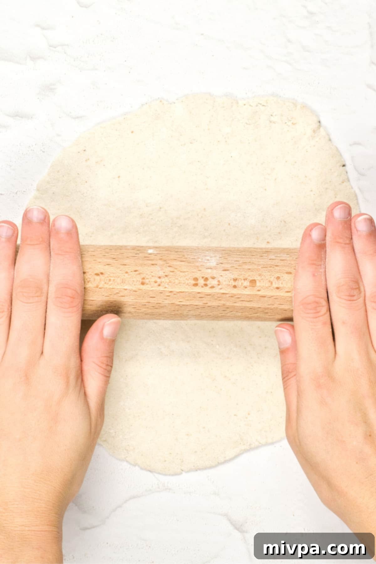 GF Pita Bread Recipe (Dairy-Free, Vegan) A rolling pin flattening a ball of gluten-free pita bread dough into a circular shape.