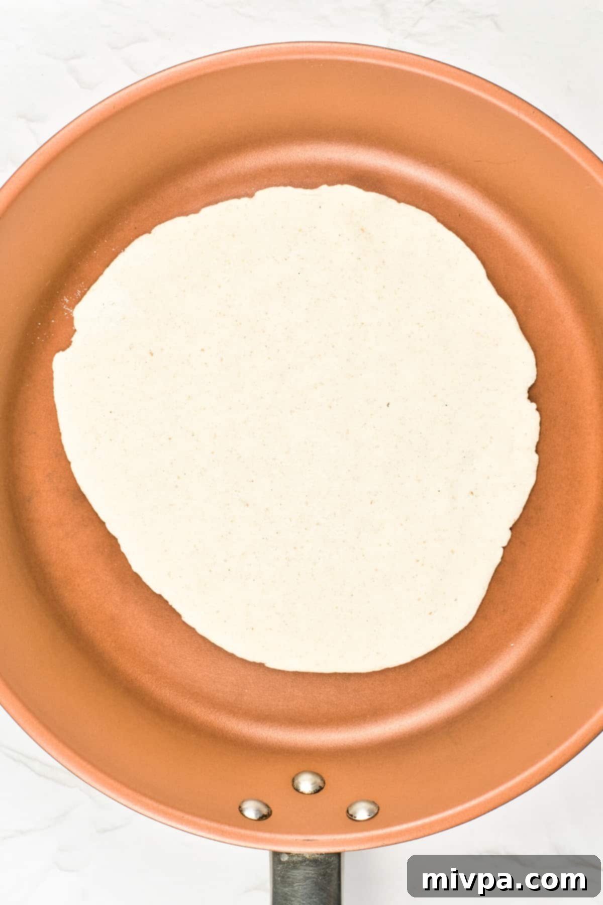 Gluten-Free Pita Bread Recipe (Dairy-Free, Vegan) A gluten-free pita cooking in a hot skillet, with bubbles beginning to form on its surface.