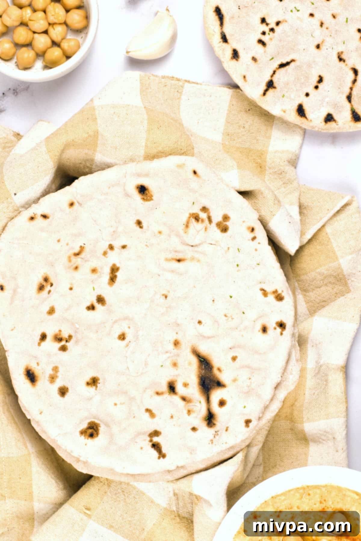Gluten-Free Pita Bread Recipe (Dairy-Free, Vegan) A stack of warm gluten-free pitas covered with a kitchen towel to maintain warmth and softness.