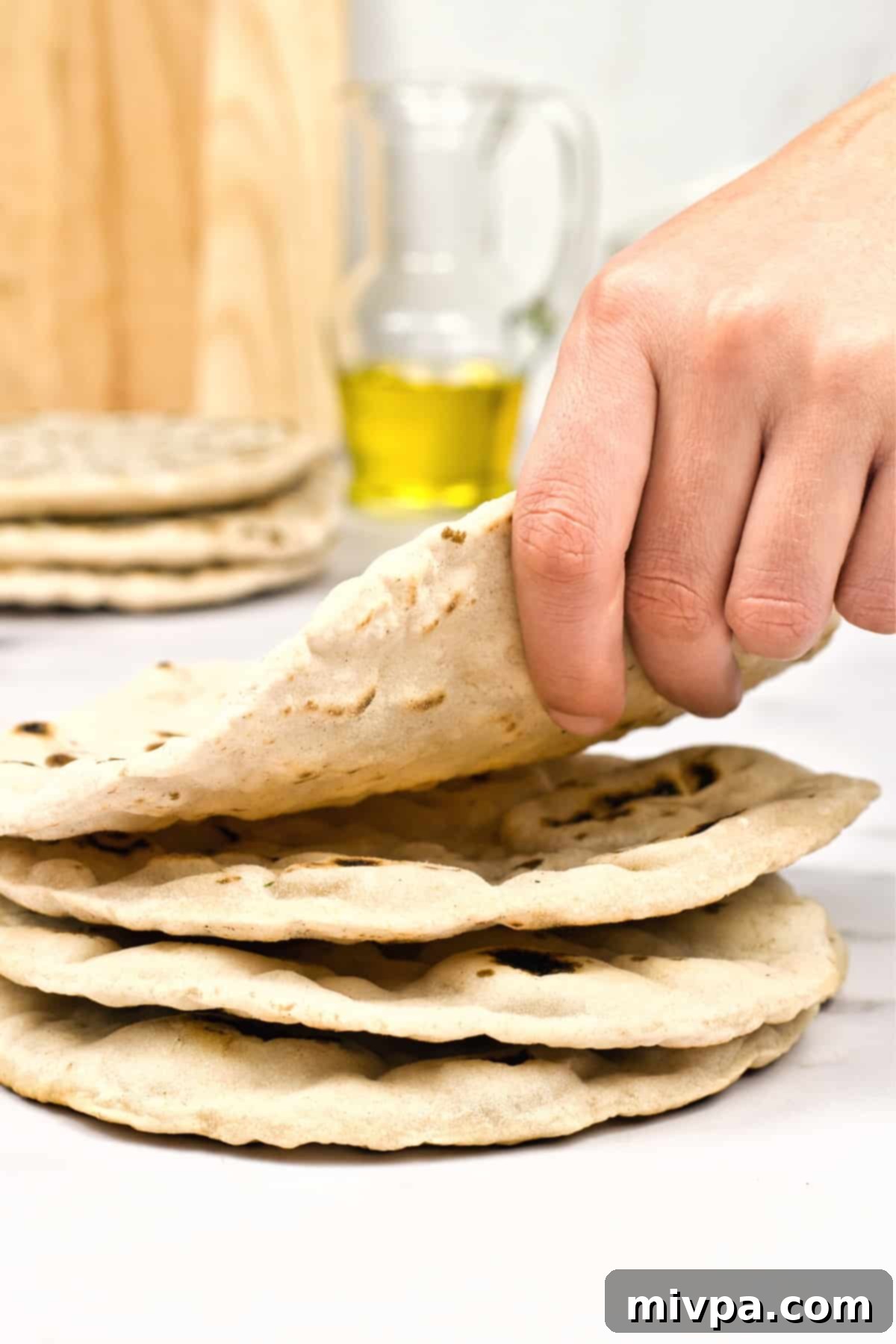 Gluten-Free Vegan Pita Bread Recipe (Dairy-Free) A hand holding up a perfectly puffed gluten-free pita bread, ready to be filled.