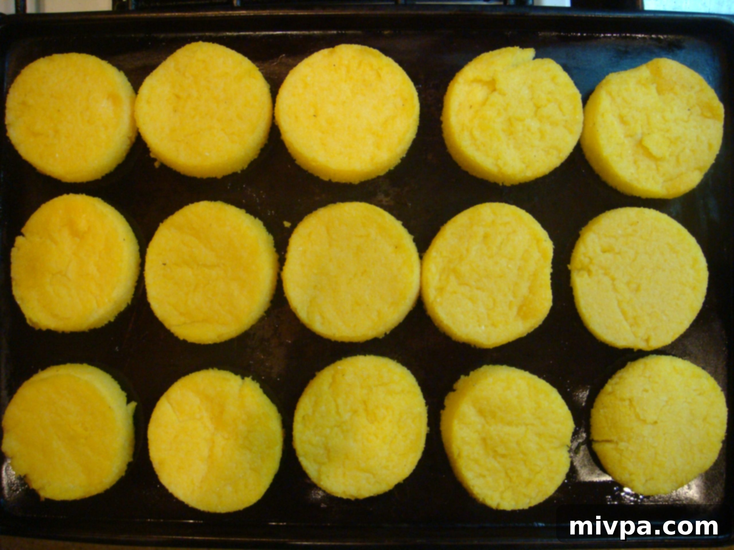 Golden Baked Polenta Bruschetta A close-up of golden-brown, baked polenta bruschetta rounds, showing their crispy crust and perfectly baked texture.