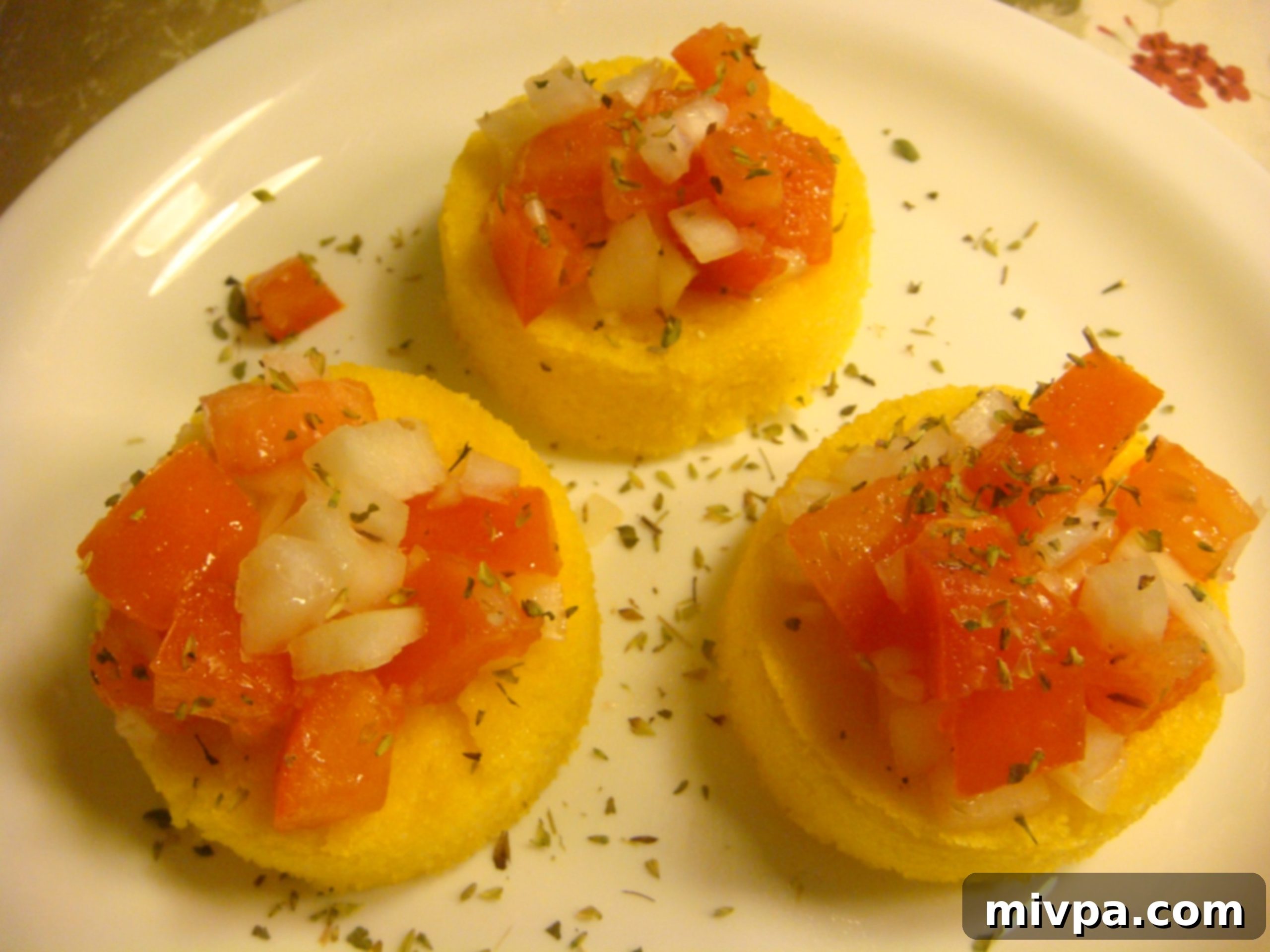 Serving Polenta Bruschetta with Topping Baked polenta bruschetta rounds generously topped with the vibrant tomato-onion mixture and sprinkled with dried oregano, ready to be served.
