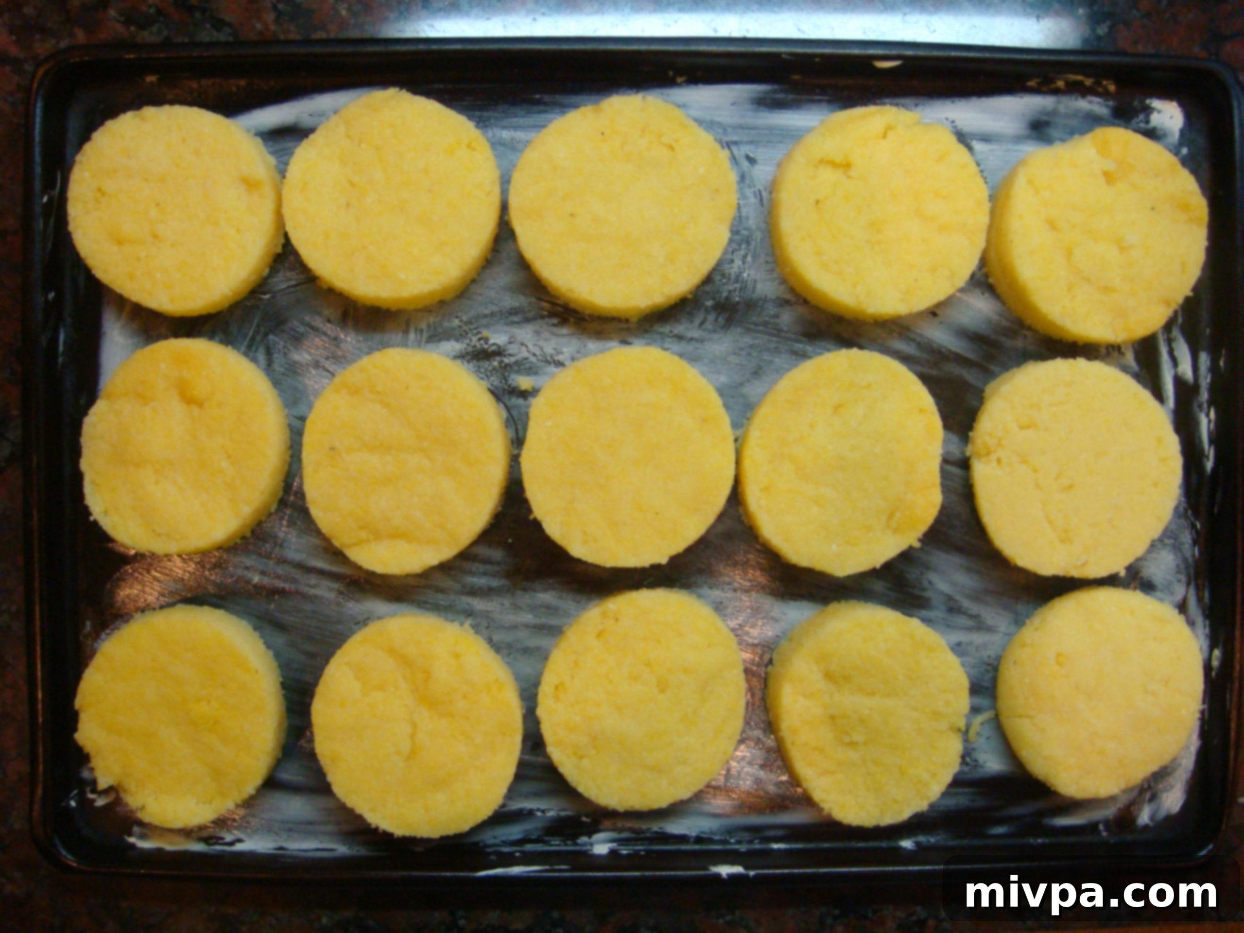 Cutting Polenta Circles Hardened polenta being cut into perfect circular shapes using a cookie cutter, with some circles already placed on a baking tray.