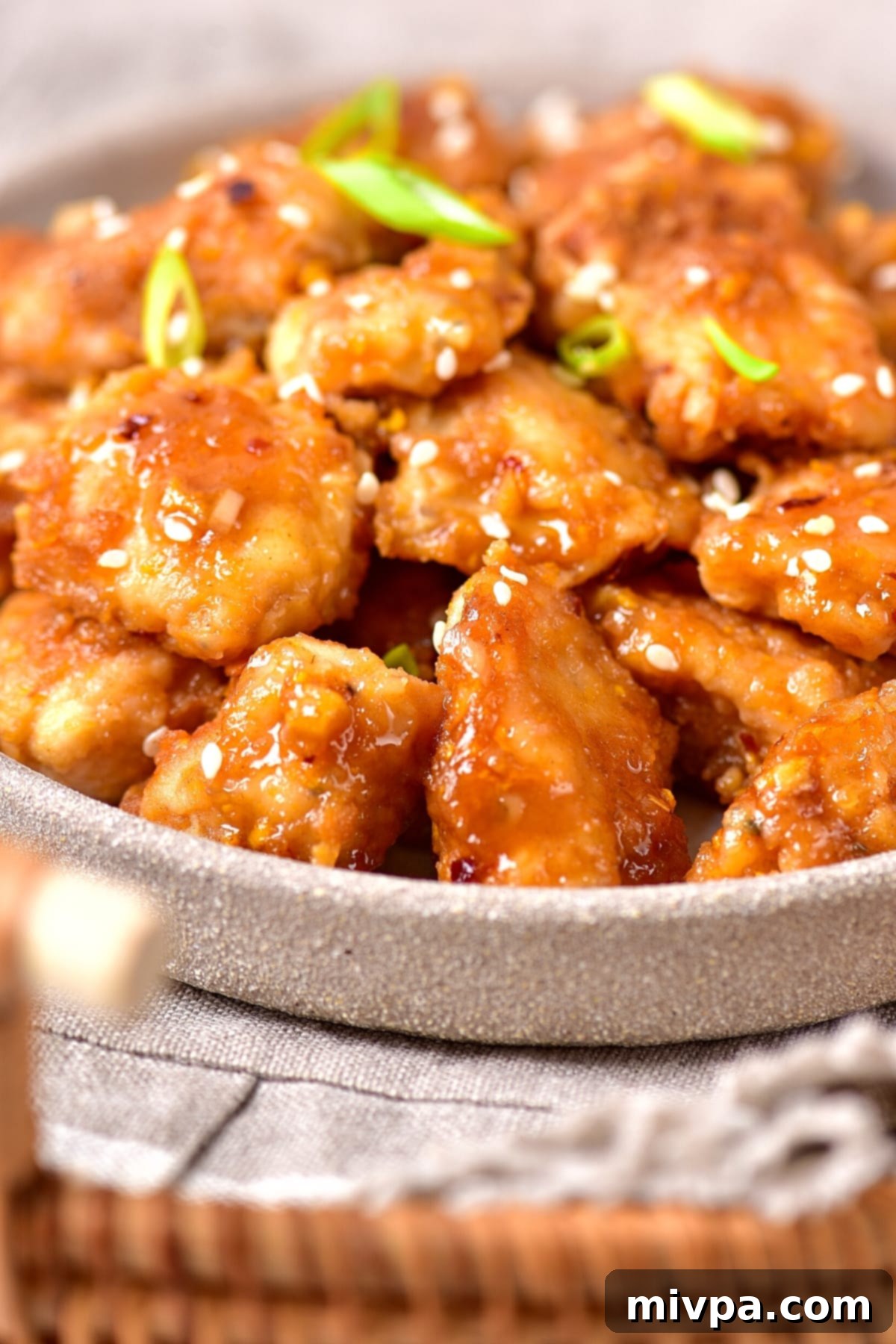 Easy Gluten-Free Orange Chicken (Dairy-Free) A plate of perfectly cooked gluten-free orange chicken garnished with sesame seeds and green onions, resting on a rustic napkin.