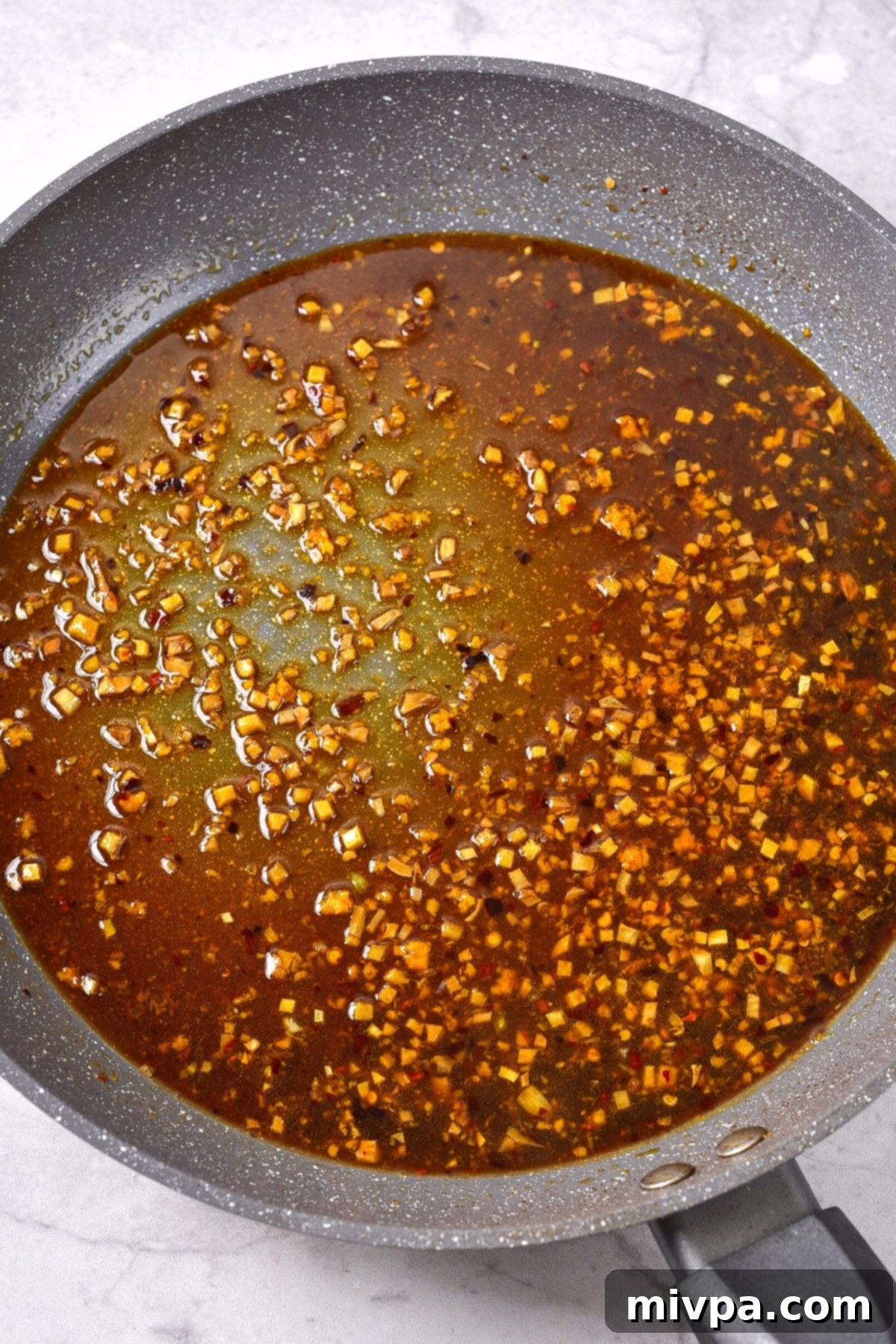 Easy Gluten-Free Orange Chicken (Dairy-Free) Various wet ingredients for the gluten-free orange chicken sauce being combined in a skillet, simmering gently.