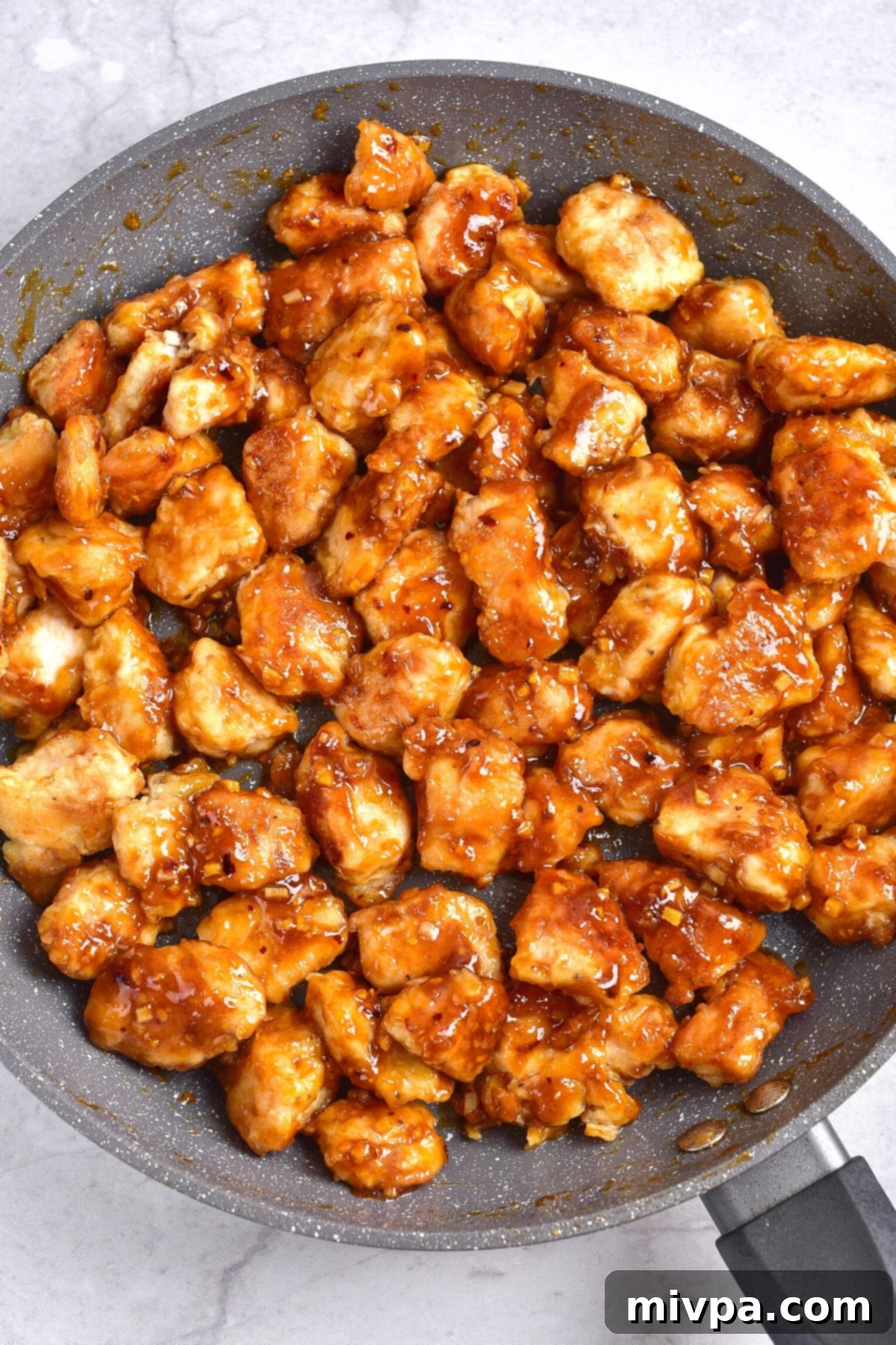 Easy GF Orange Chicken Recipe A large skillet brimming with crispy orange chicken pieces, all beautifully coated in a thick, glossy orange sauce.