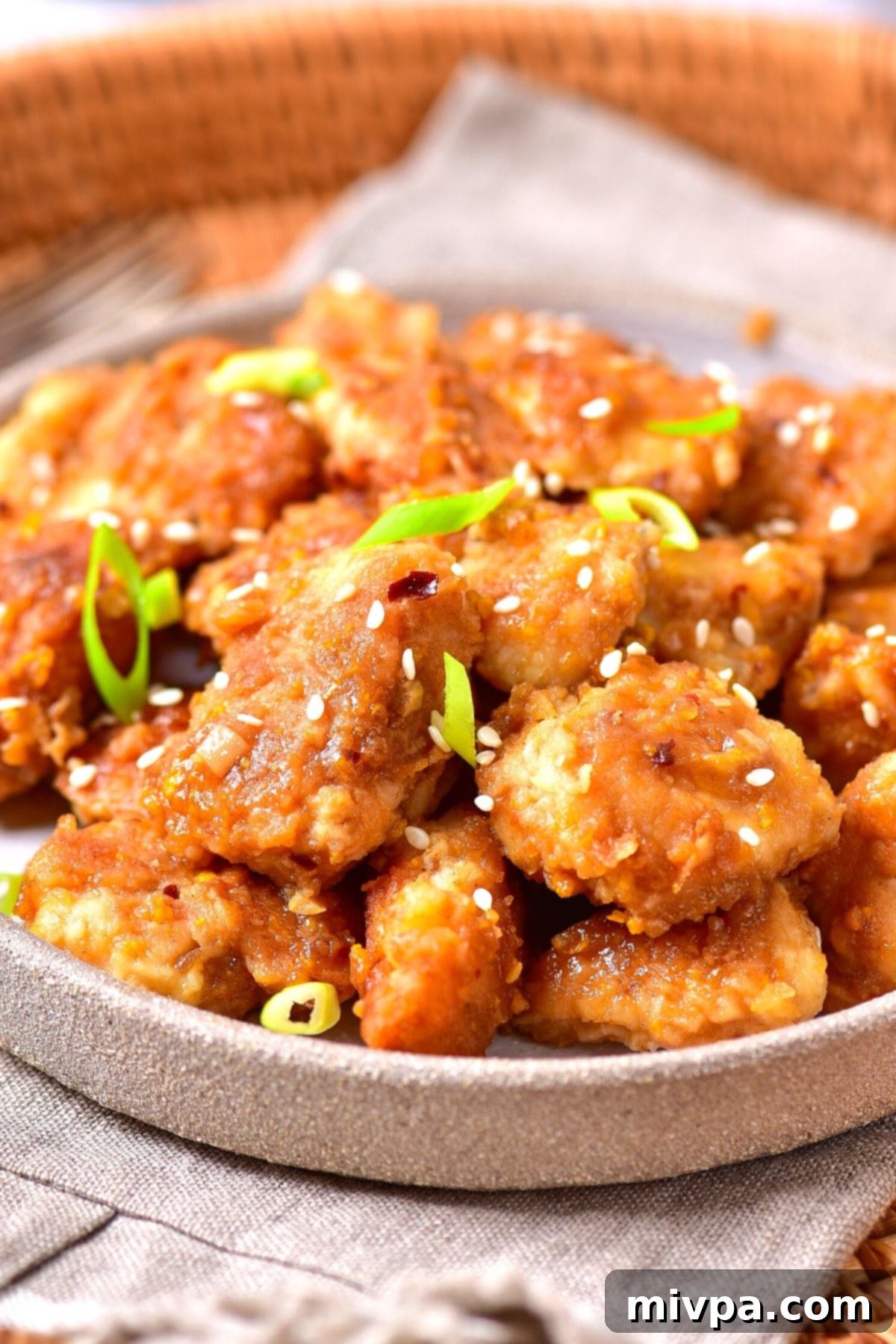Gluten-Free Orange Chicken Recipe (Dairy-Free) A beautifully plated serving of gluten-free dairy-free orange chicken, garnished with sesame seeds and green onions, presented on a napkin.