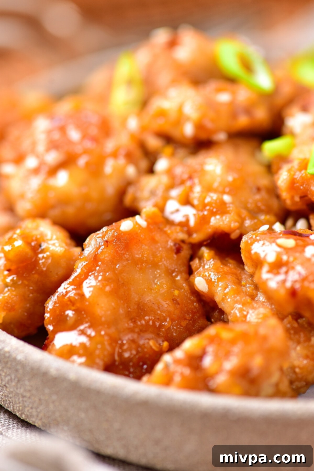 Gluten-Free Dairy-Free Orange Chicken An inviting close-up of orange chicken, garnished with glistening sesame seeds and vibrant green onions, showcasing its rich texture and appealing glaze.