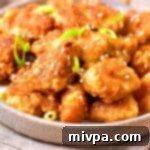 Simple Gluten Free Dairy Free Orange Chicken 2 A close-up of crispy gluten-free orange chicken in a bowl, garnished with green onions and sesame seeds.